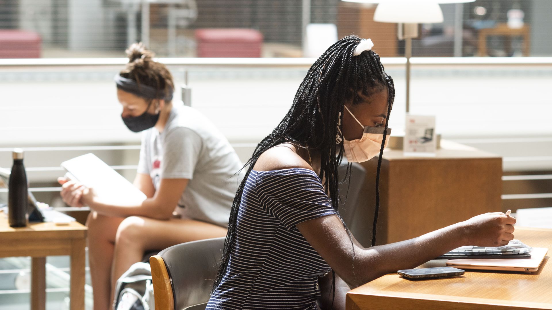 Two college students read wearing masks.
