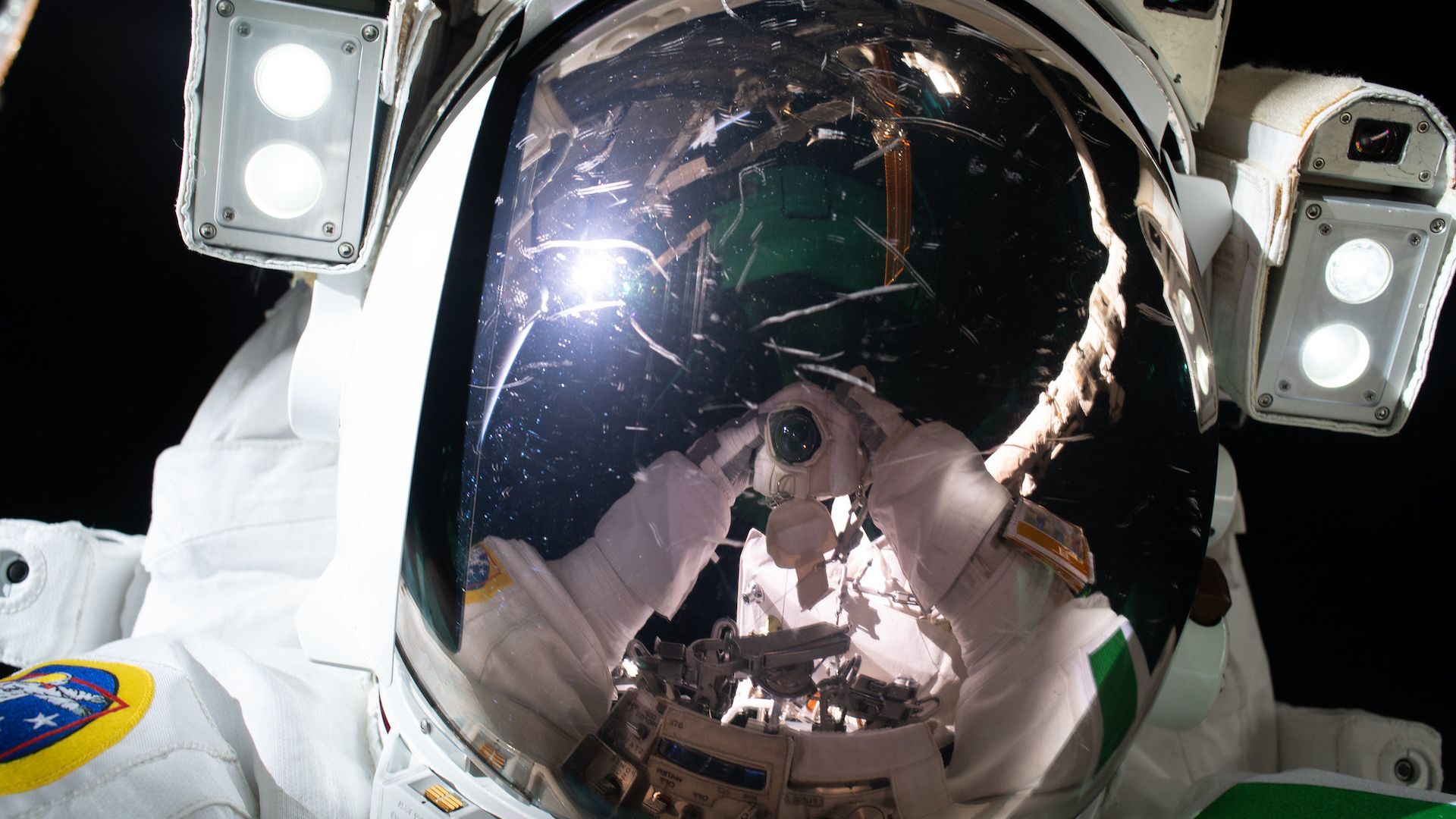 An astronaut's visor reflects a camera as he holds it up to take a selfie in space