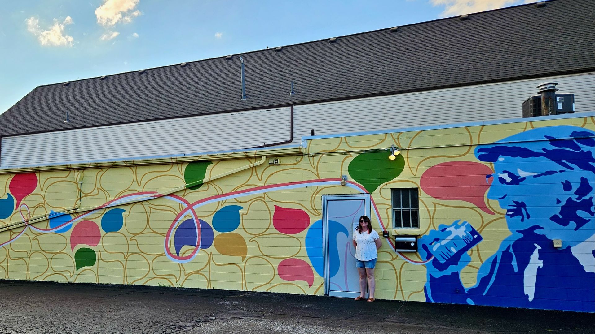 Alissa standing in front of a multicolored mural with a man speaking into a tin can