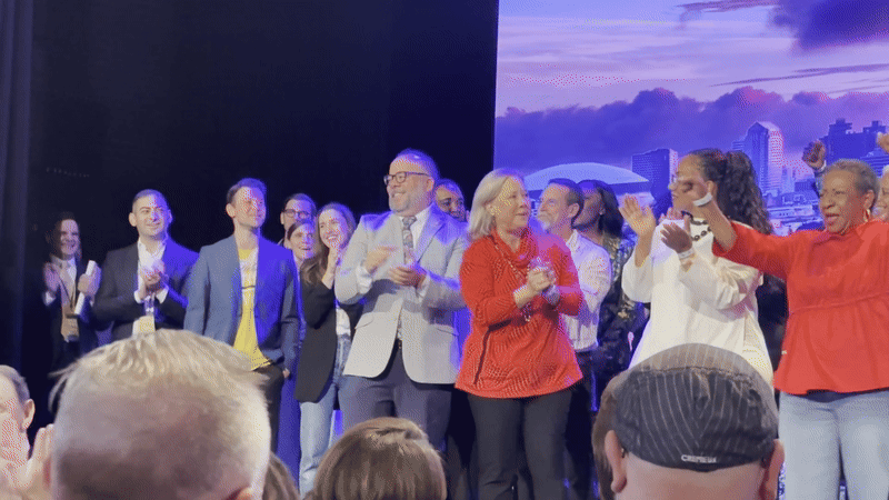 A diverse group of people applaud onstage.