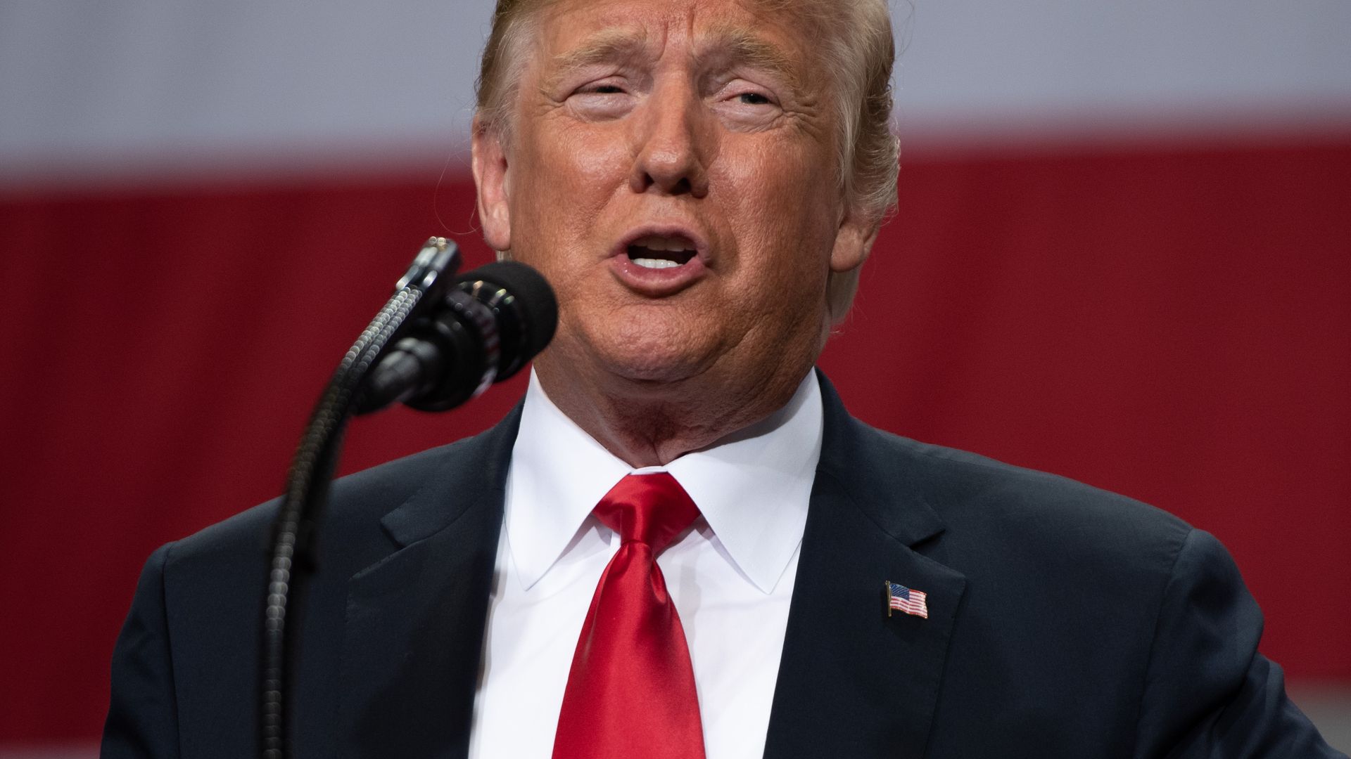 Donald Trump smiles and purses his lips while speaking into a microphone