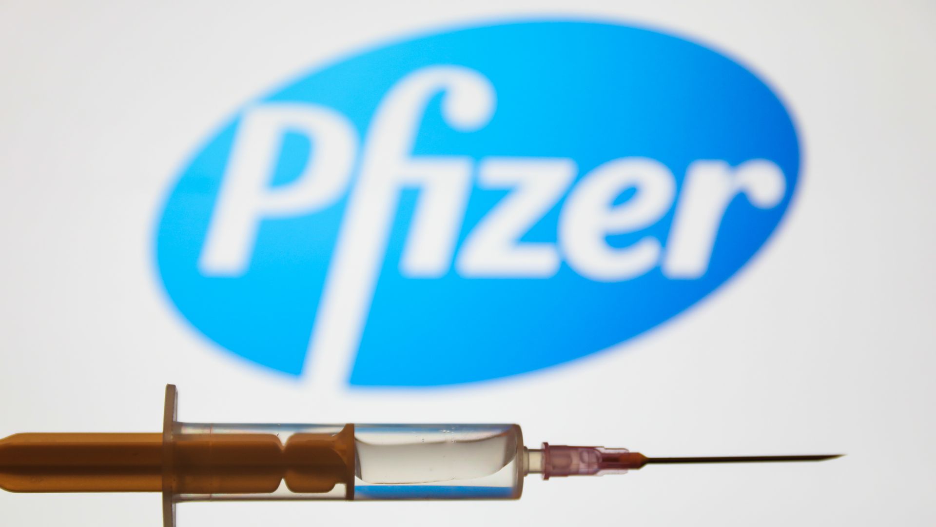 Pfizer's blue logo in the background, and a vaccine syringe in the foreground.