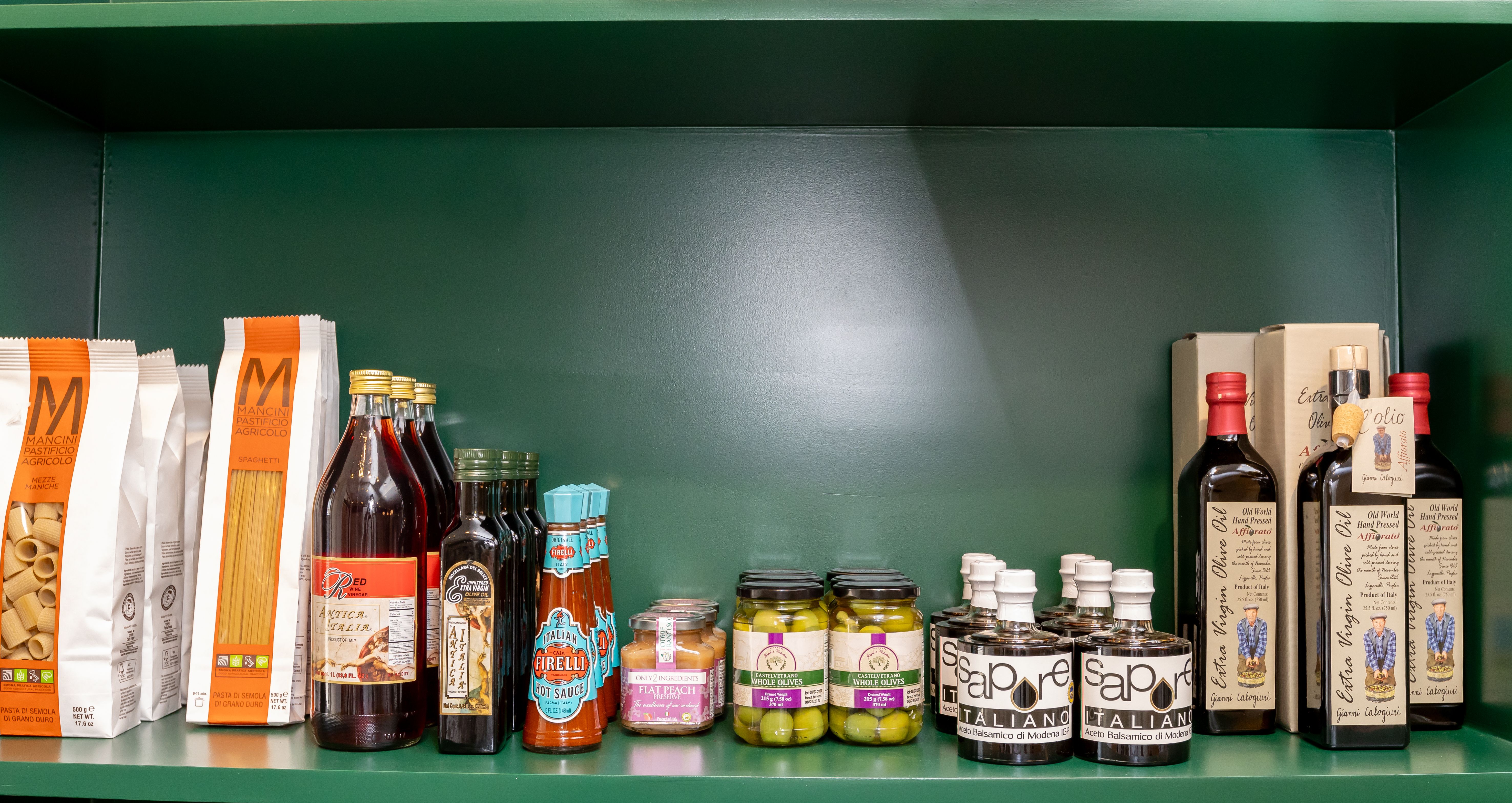 Italian pantry goods like pasta and olive oil on a green shelf