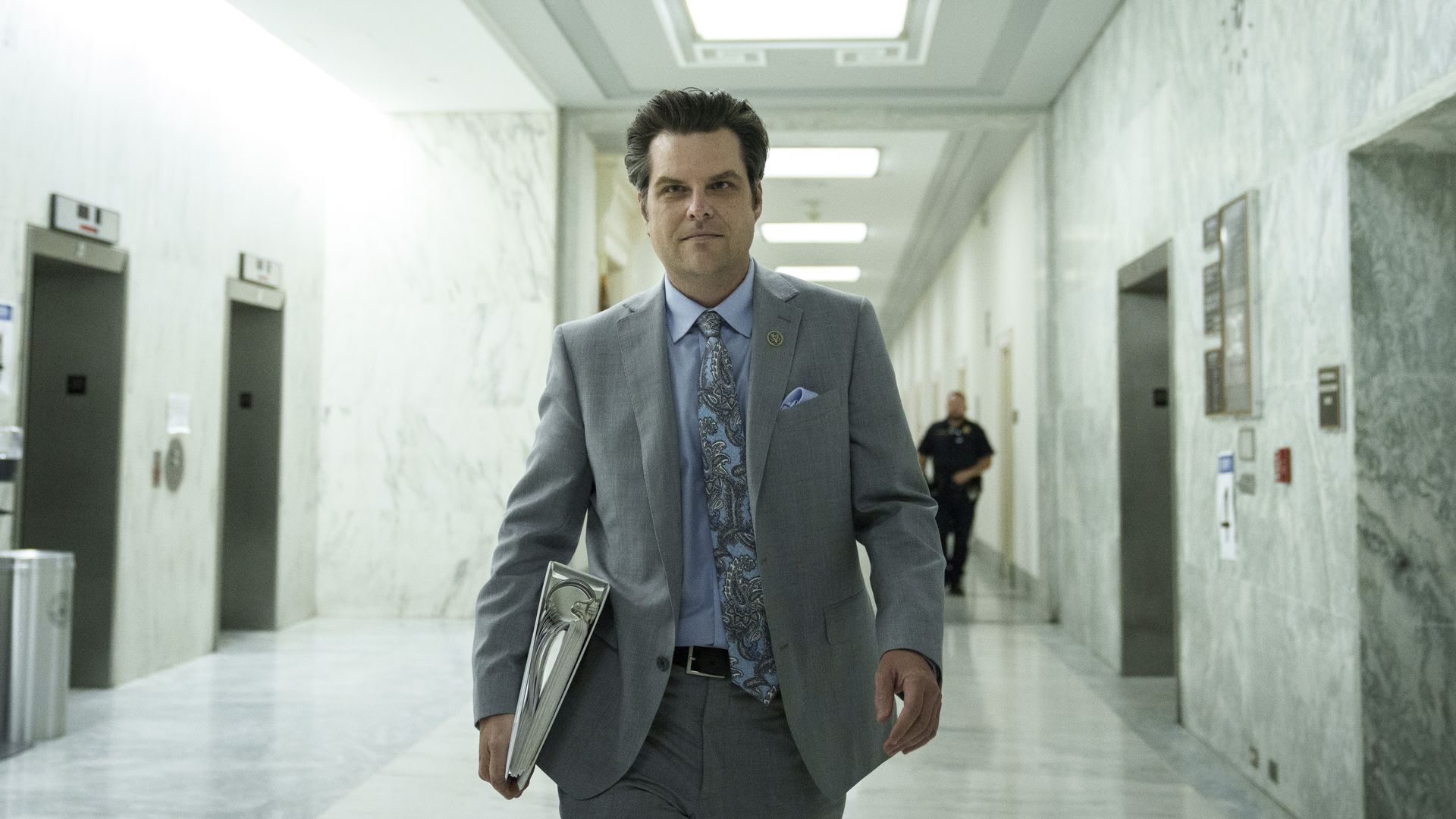 Matt Gaetz walks through a hallway on Capitol Hill with a binder in one hand.