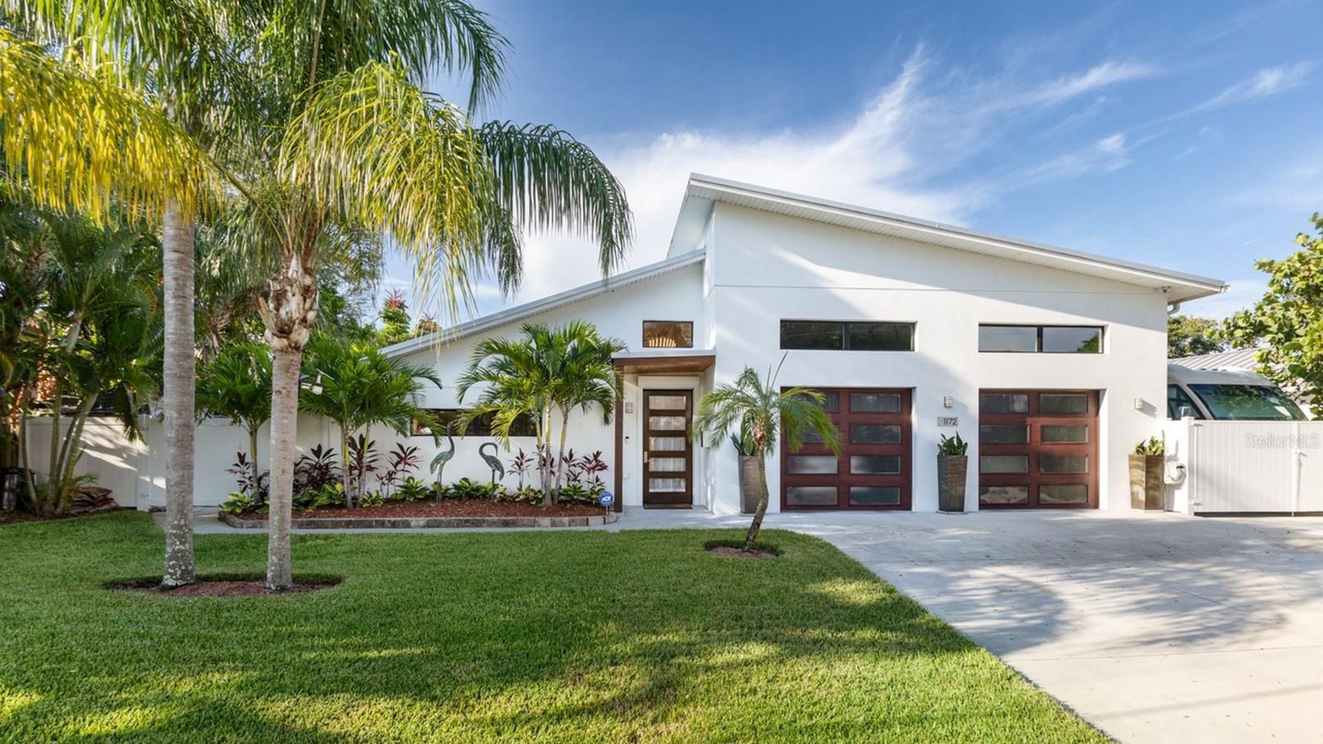 A one-level white modern house with a slanted roof withe a two-car garage with wooden doors with many windows..