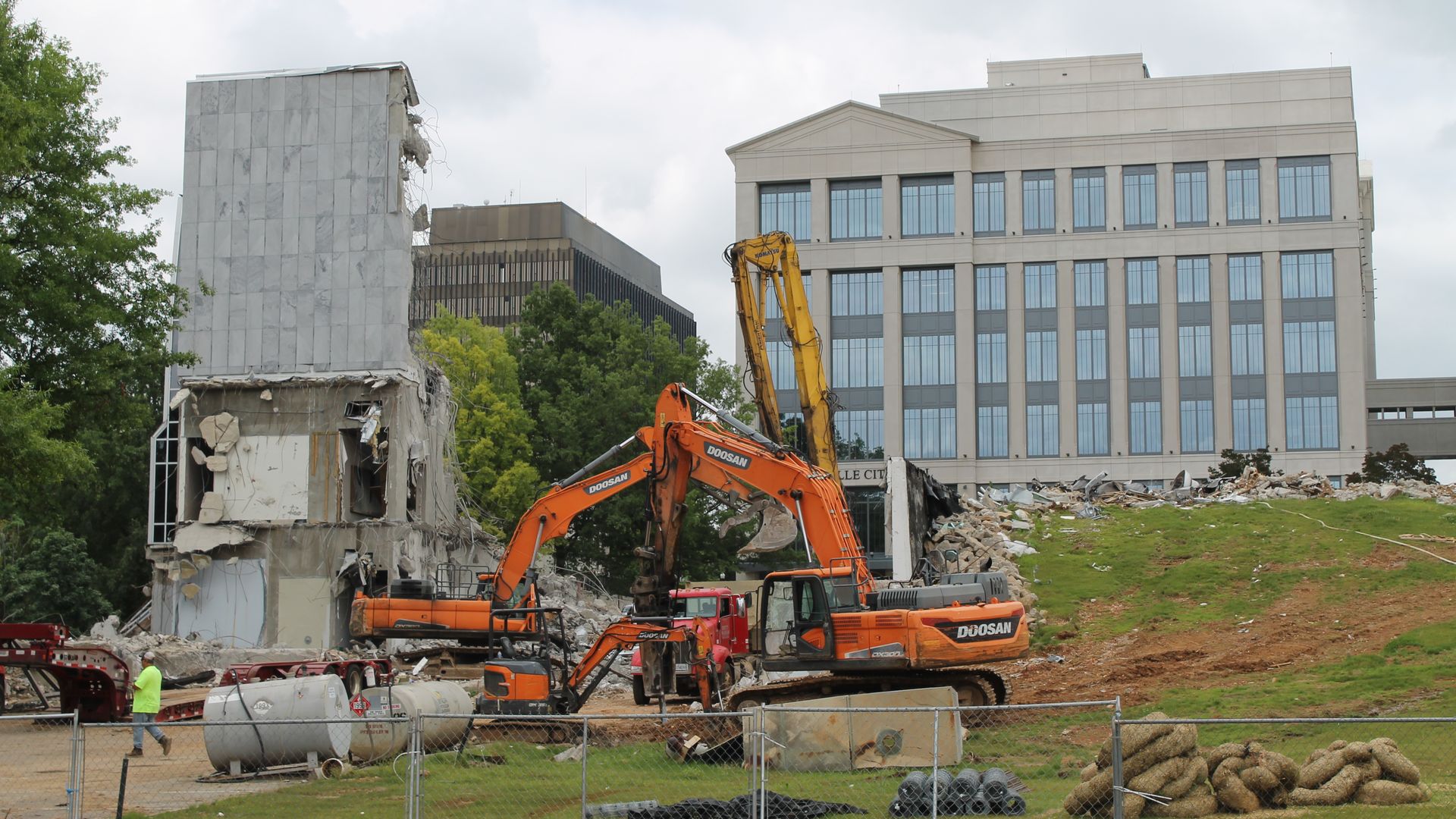 A building, the former Huntsville City Hall, is being demolished by two bulldozers. The new city hall can be seen in the background.