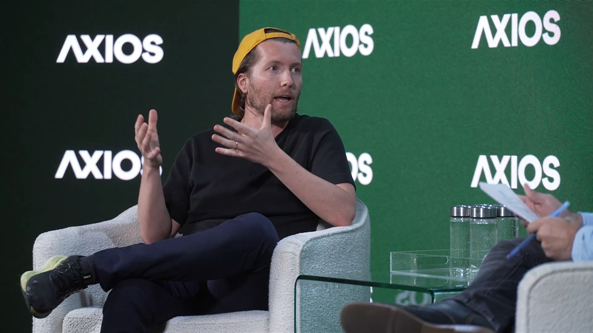 Clem Delangue, seated, speaks in front of a green backdrop that reads "AXIOS" repeatedly in white text. 