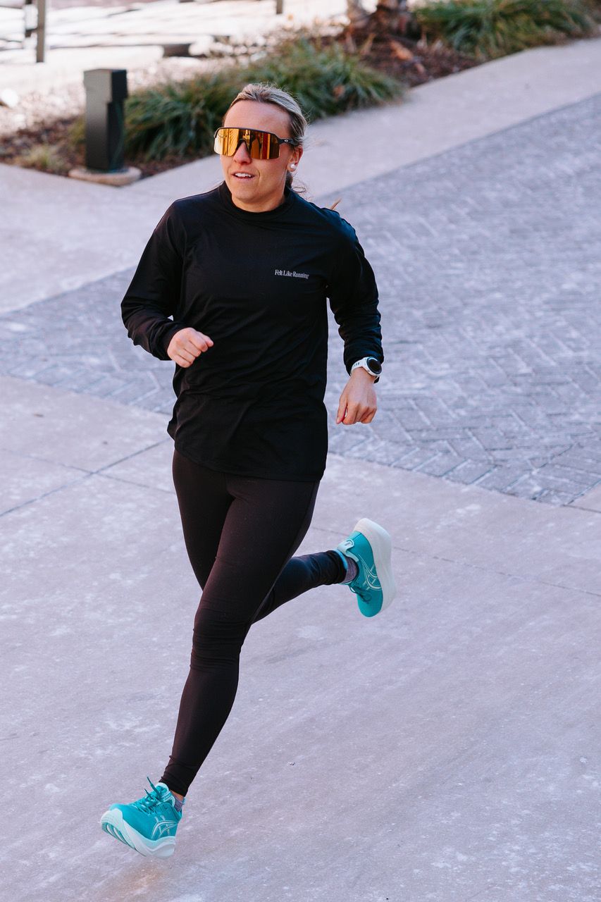 A woman running in a black shirt and leggings with grey socks and turquoise Asics.  