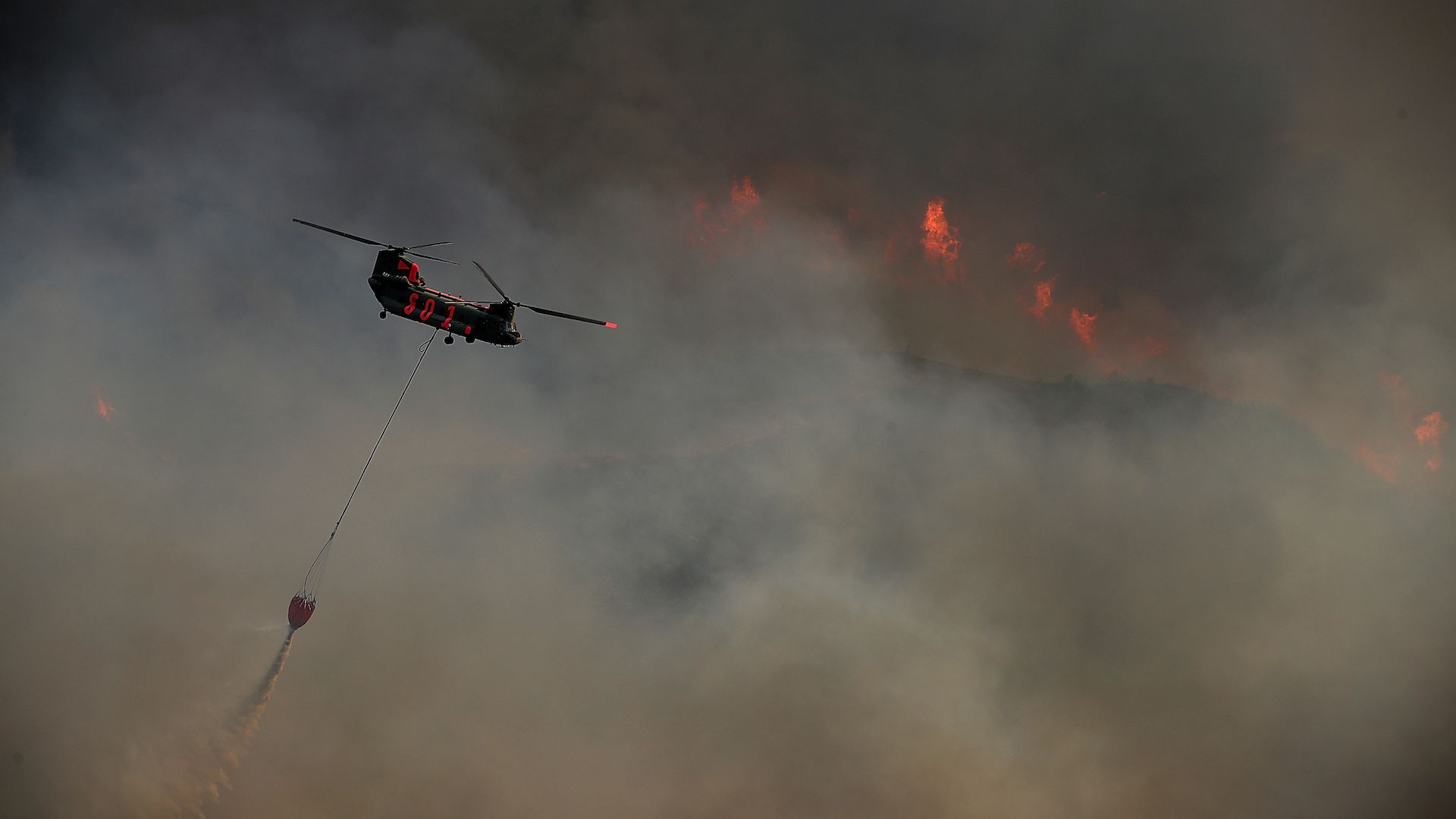 LAKEPORT, CA - JULY 31: A helicopter drops water on the River Fire as it burns through a canyon on July 31, 2018 in Lakeport, California.