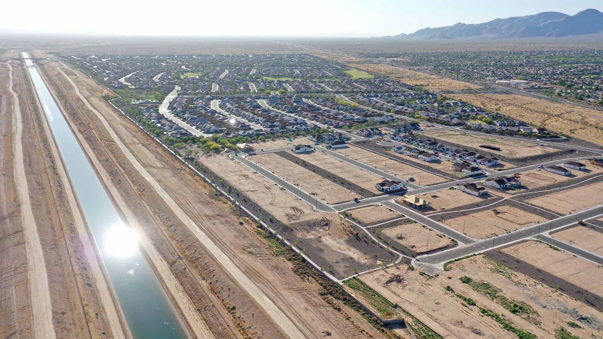 An aerial view of a canal running alongside housing subdivisions and vacant desert land.