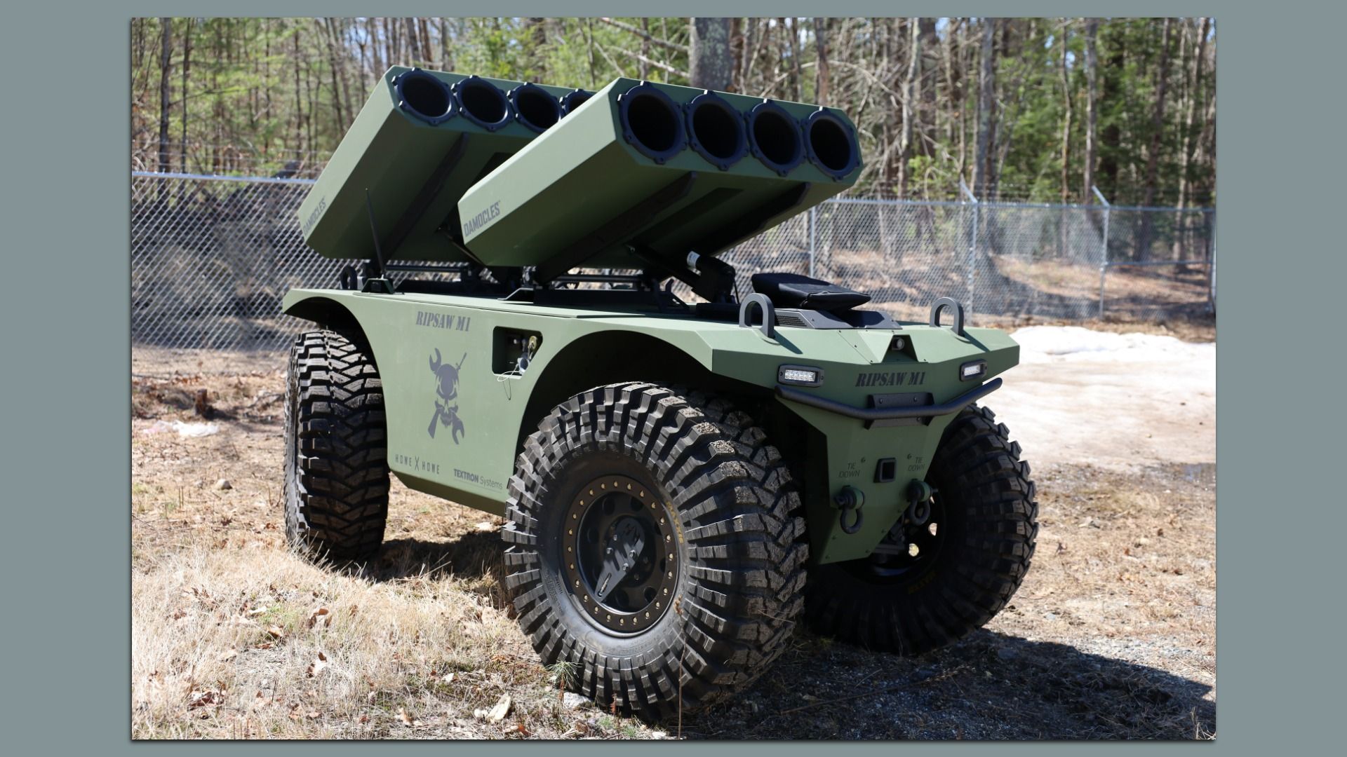 Olive-green military unmanned ground vehicle with a four-tube rocket launcher on top. It also has large rugged tires.