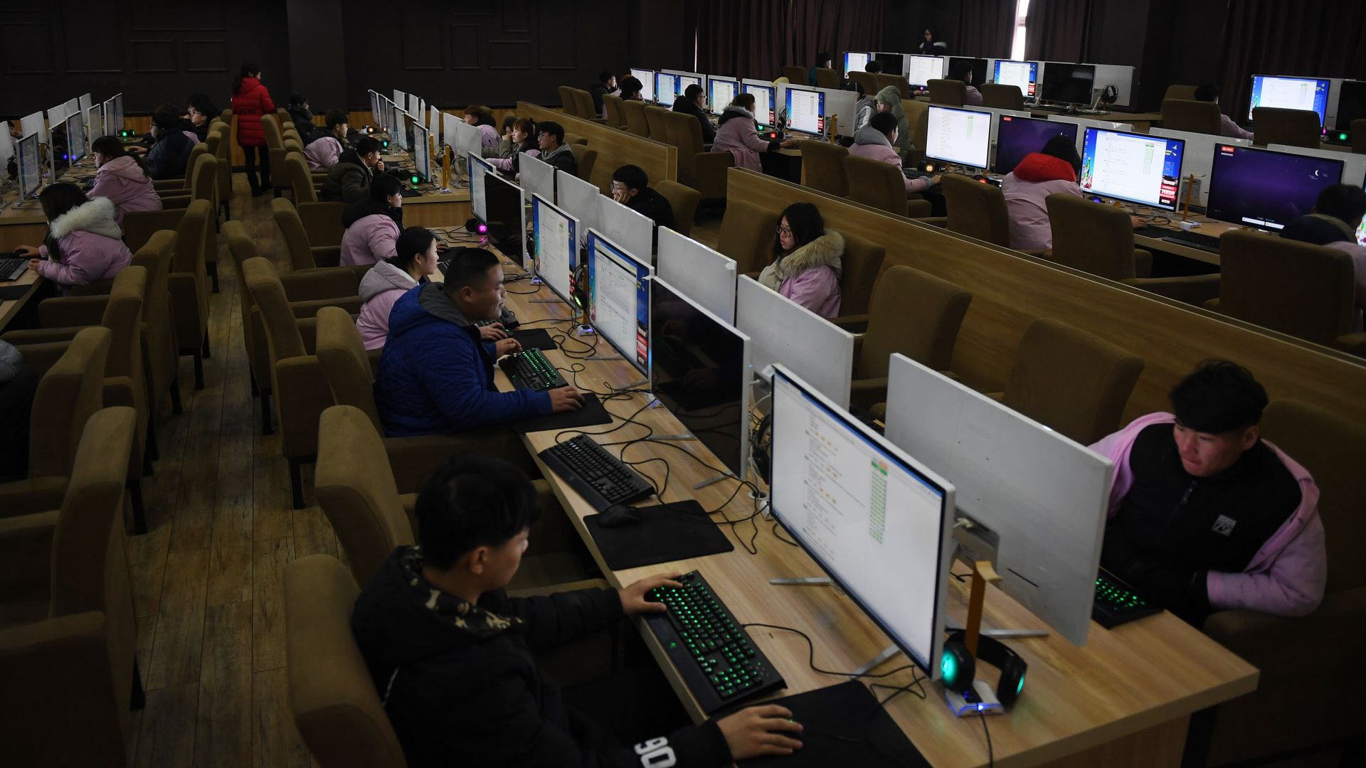 rows of people sitting at desks with desktop computers 