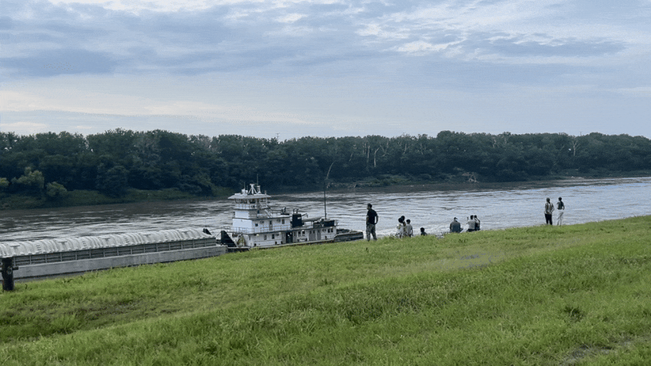 Bystanders watch and wave to a barge passing by near the bank on the Missouri River at Berkley Riverfront Park in Kansas City.