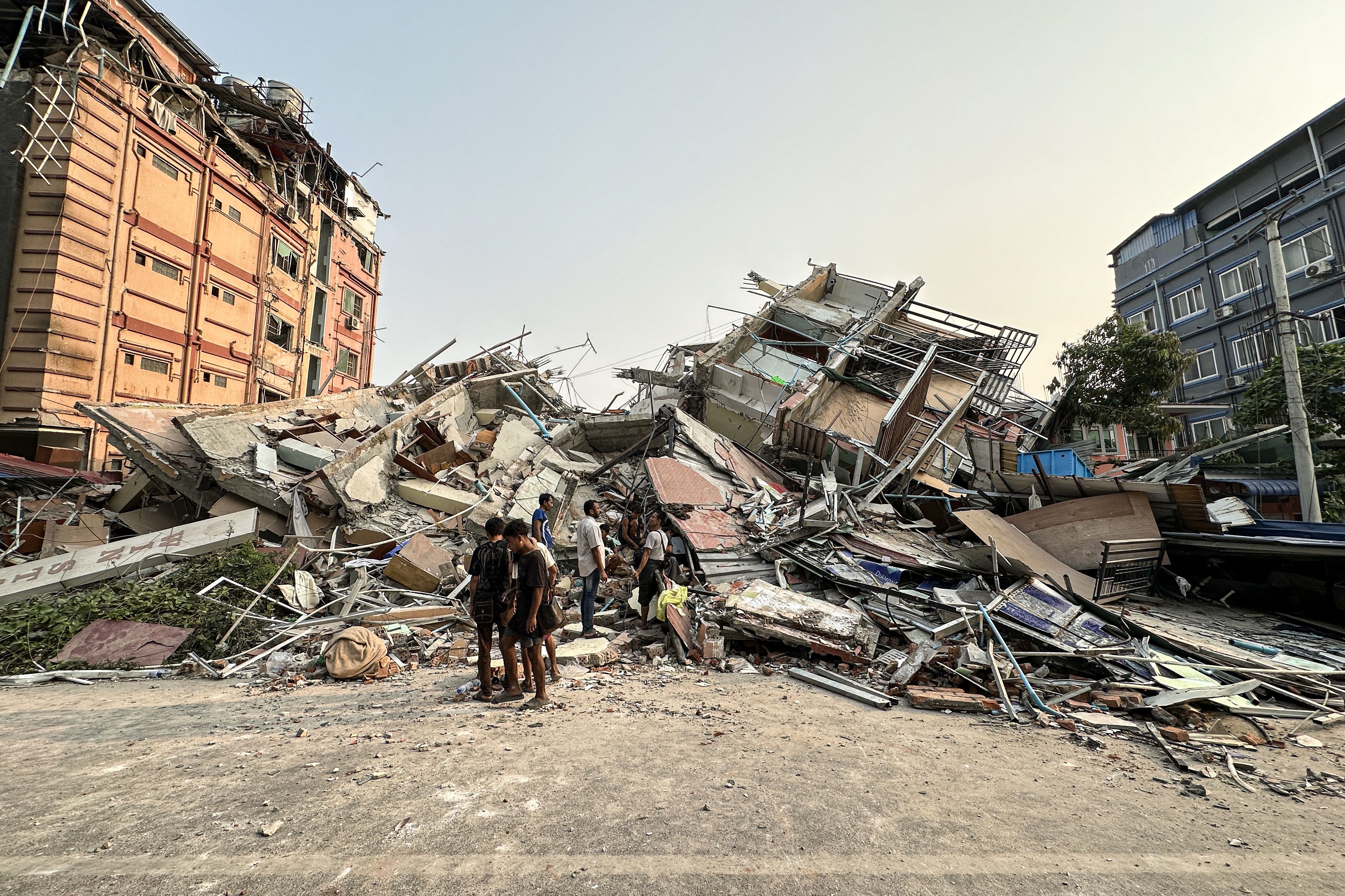 People stand past the debris of a collapsed building in Mandalay on March 28