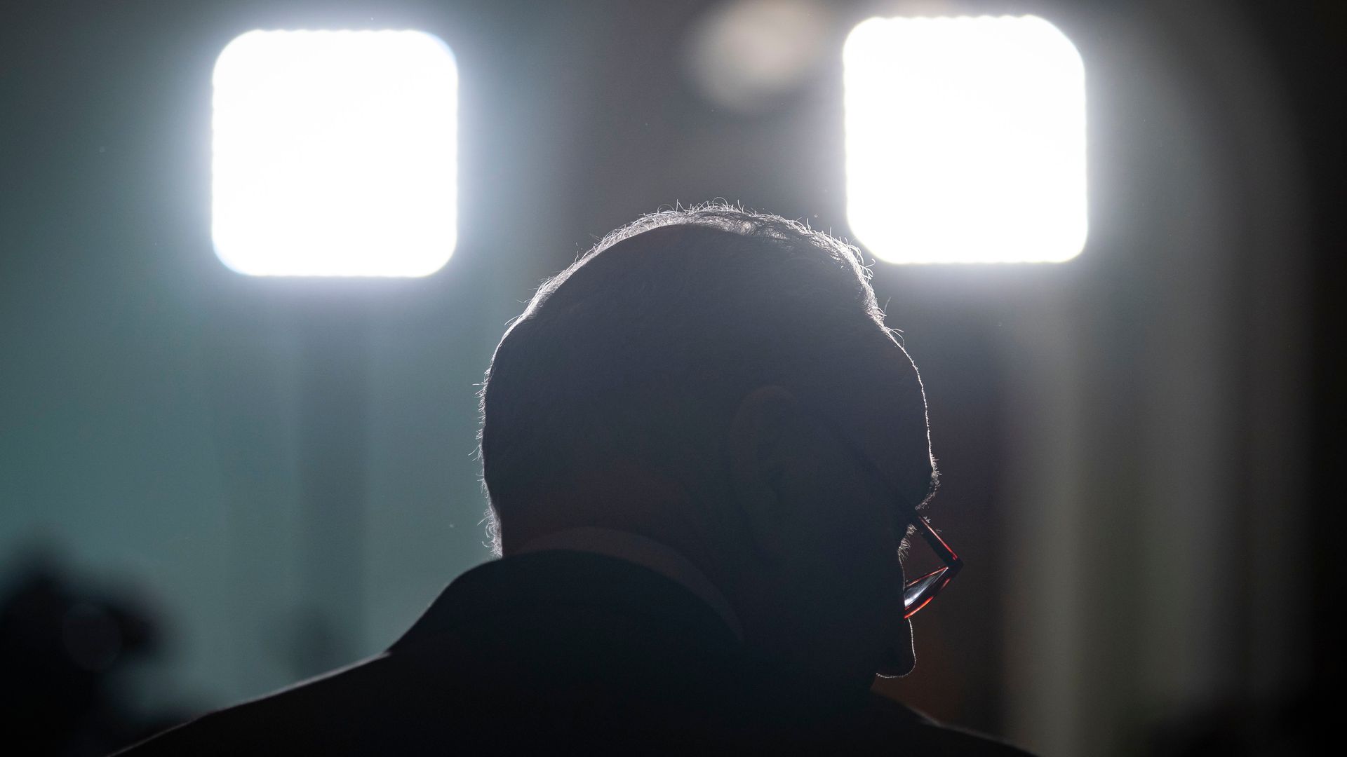 Senate Majority Leader Chuck Schumer is seen in silhouette set by television lights.