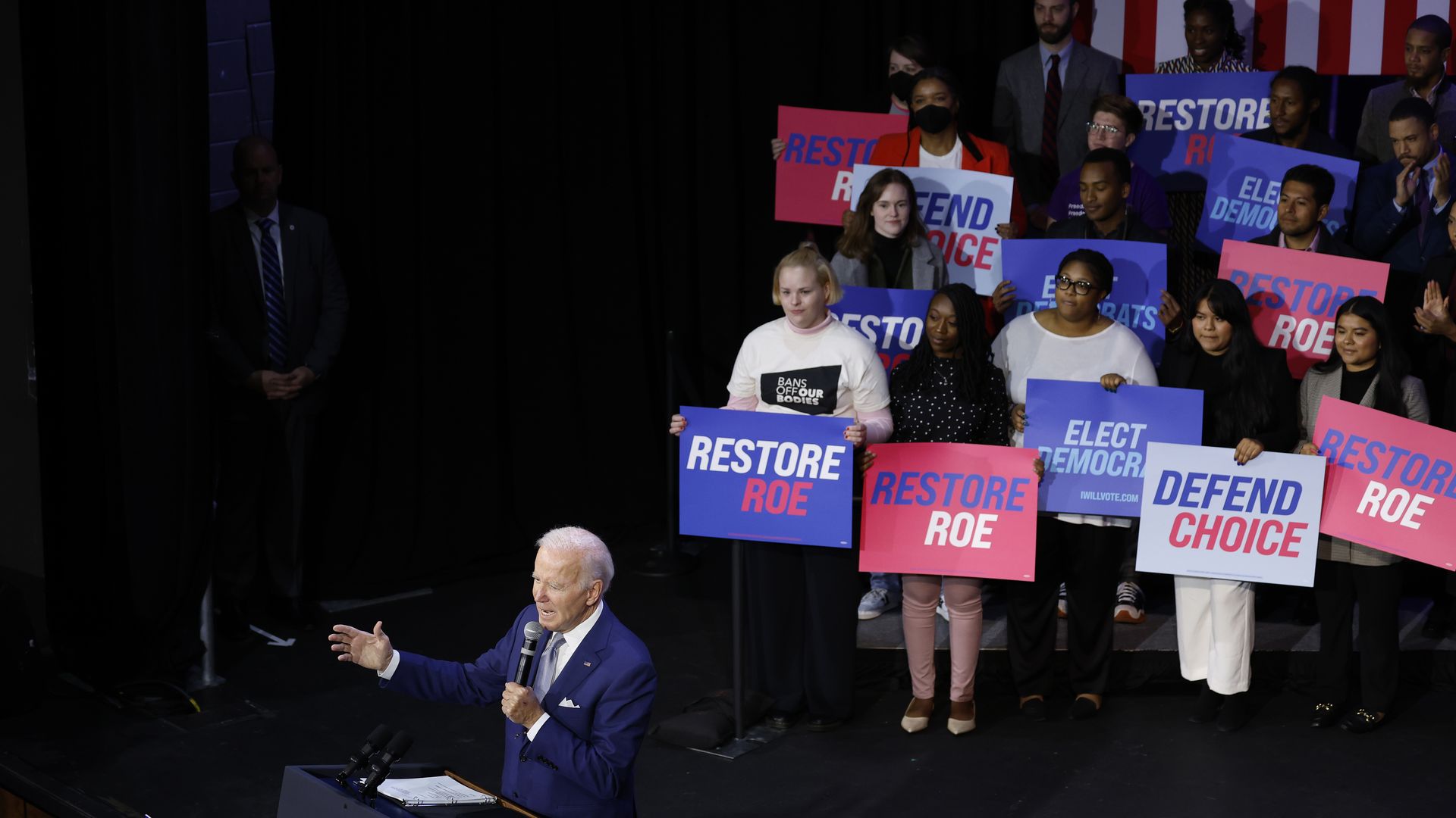 U.S. President Joe Biden speaks at a Democratic National Committee event with people behind him on stage holding pro-abortion rights signs.