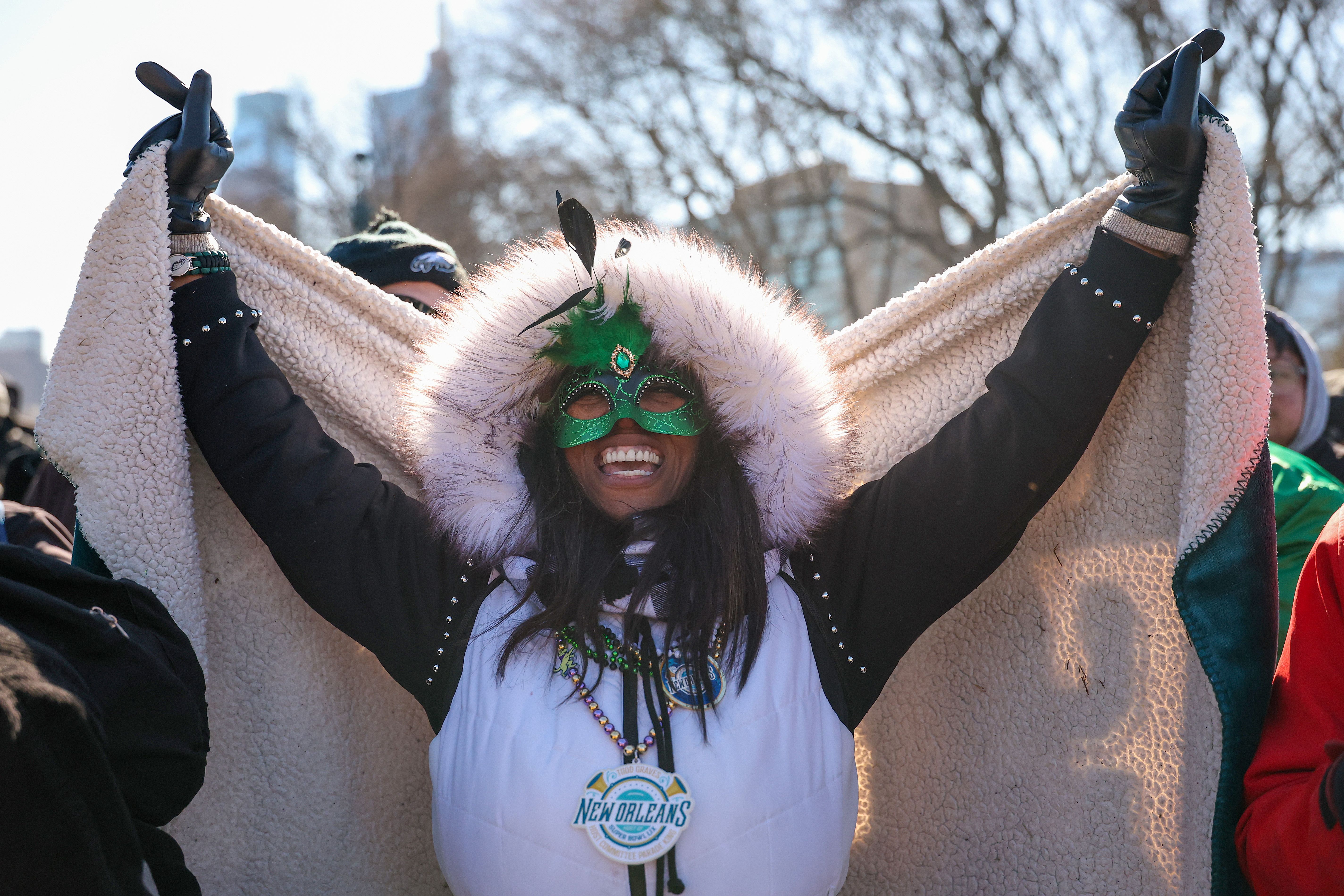 A fan holds up a blanket while smiling and wearing a Mardi Gras mask and beads.
