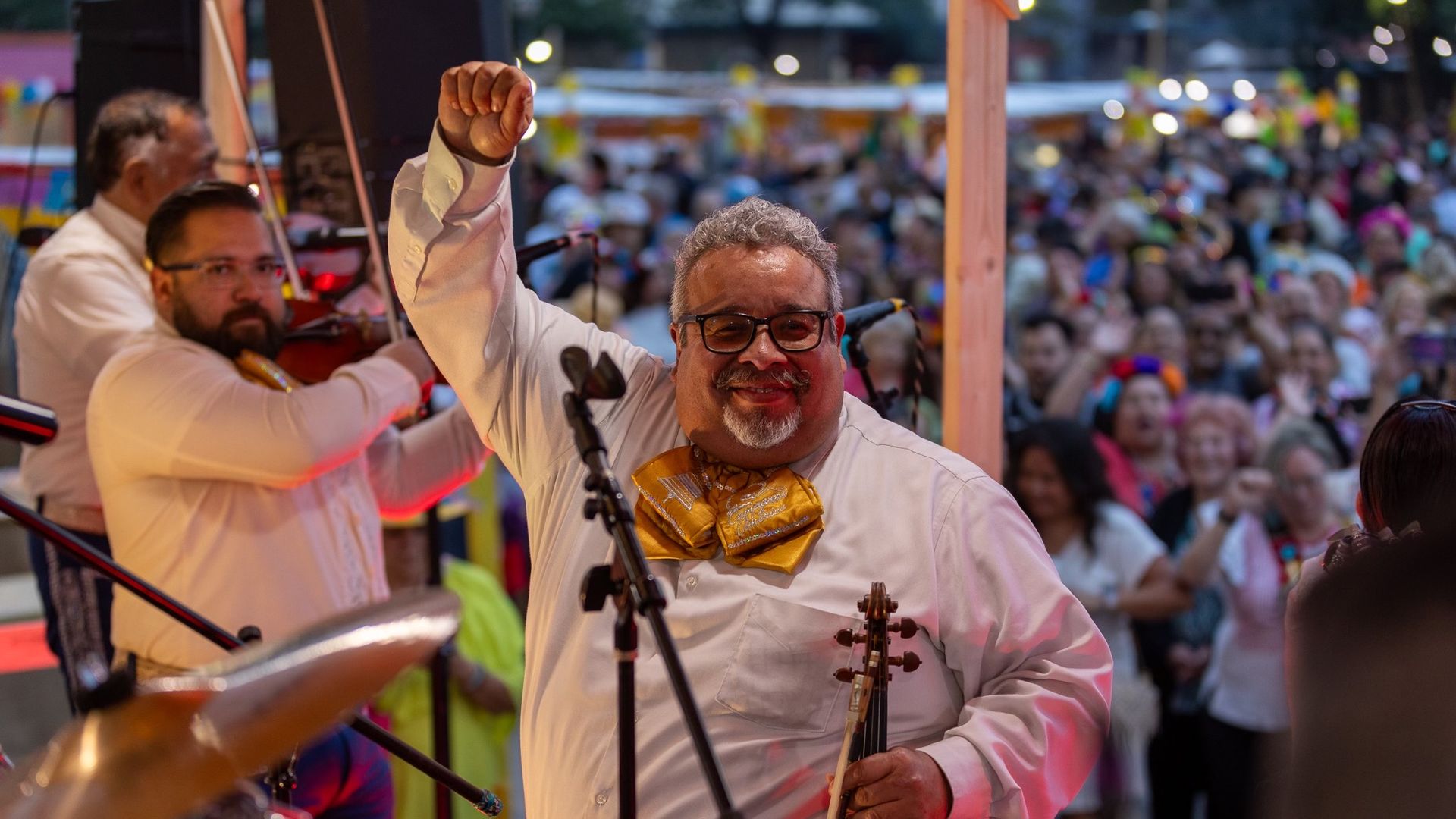 Anthony Medrando stands facing the camera smiling, with his arm up, while a crowd cheers him on.