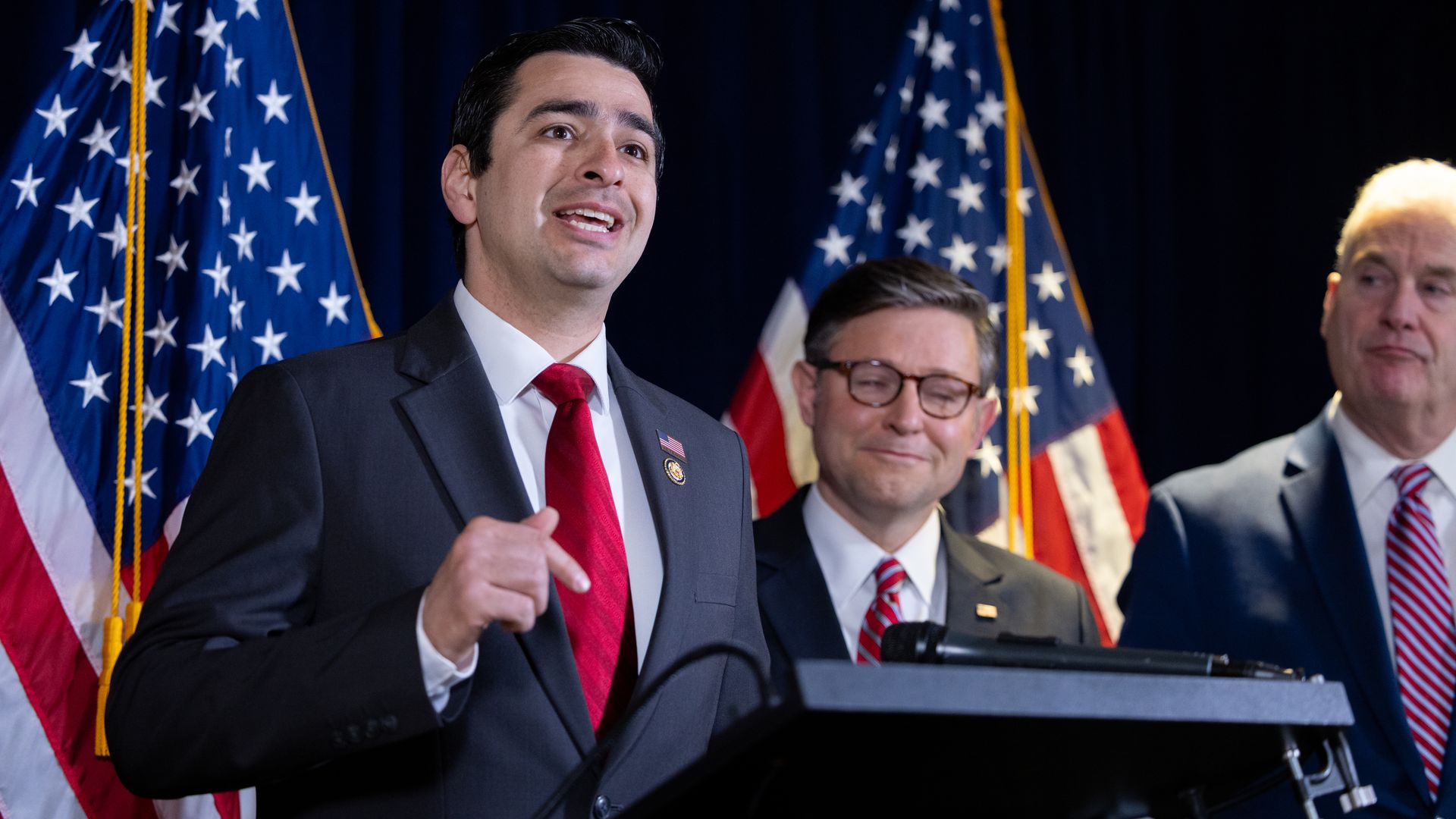A man in a suit speaks at a lectern. 