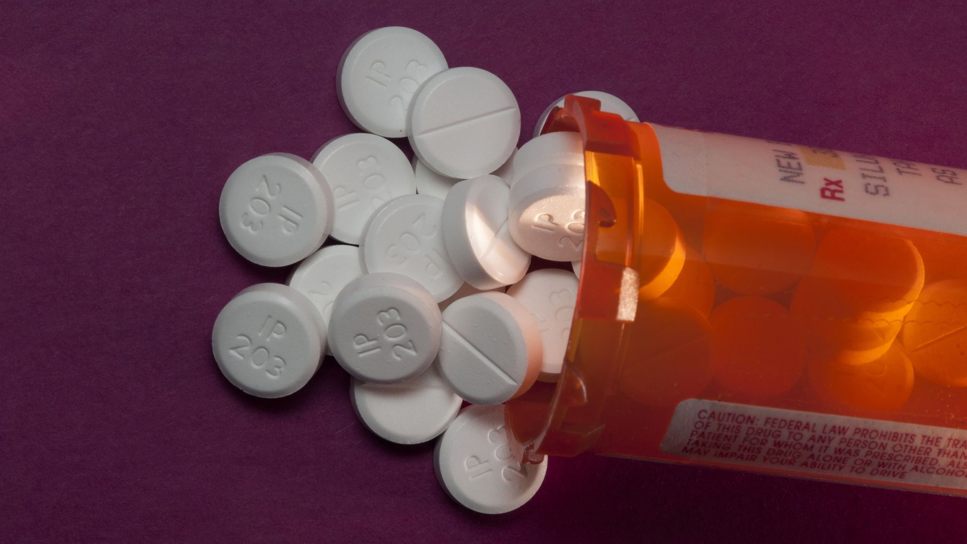 In this image, small round white oxycodone pills spill out of a prescription bottle 
