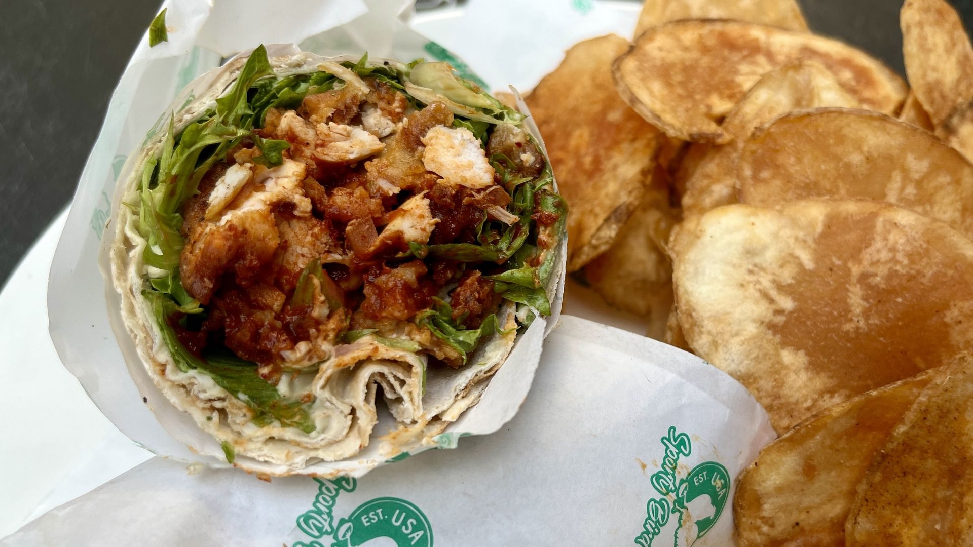 Photo of a wrap and side of potato chips on a plate. 
