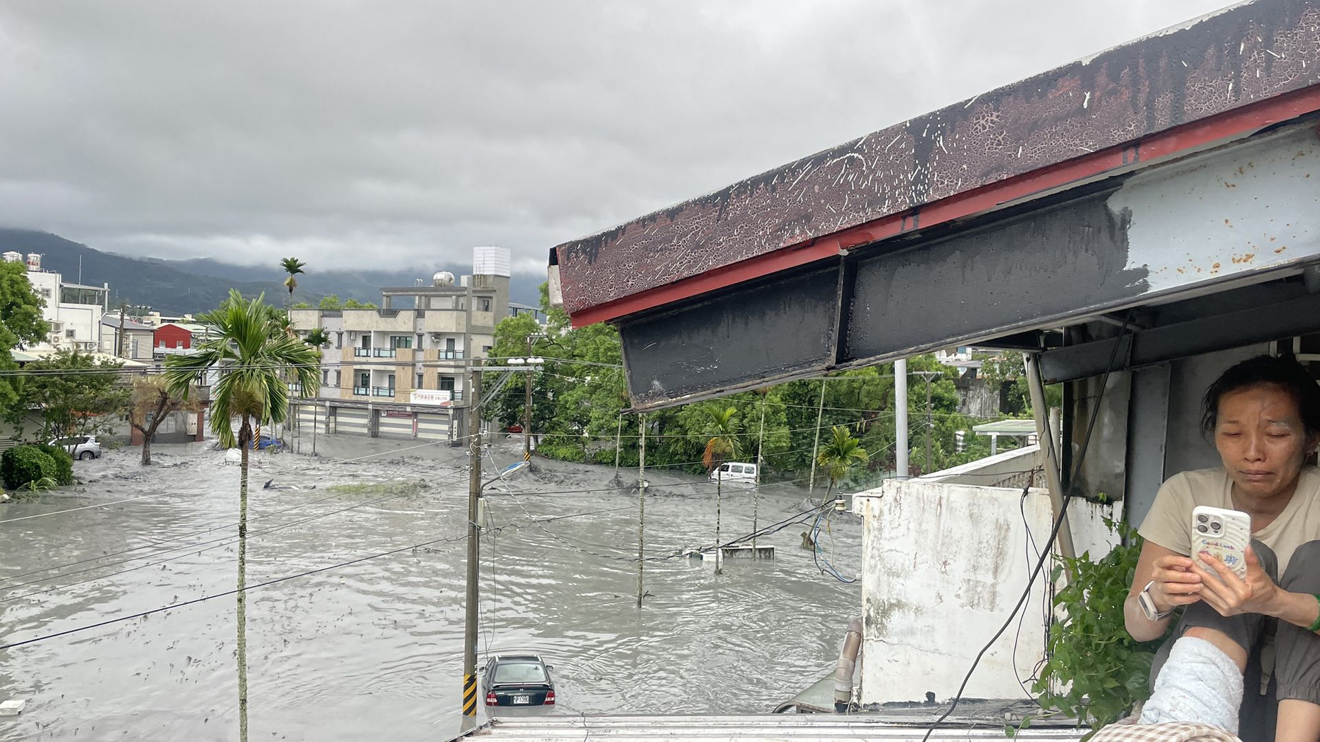 A resident uses her mobile phone while sitting on the roof of a house, as water from a burst landslide dam overflows and floods the area in Hualien on September 23, 2025, as a result of heavy rain due to Super Typhoon Ragasa