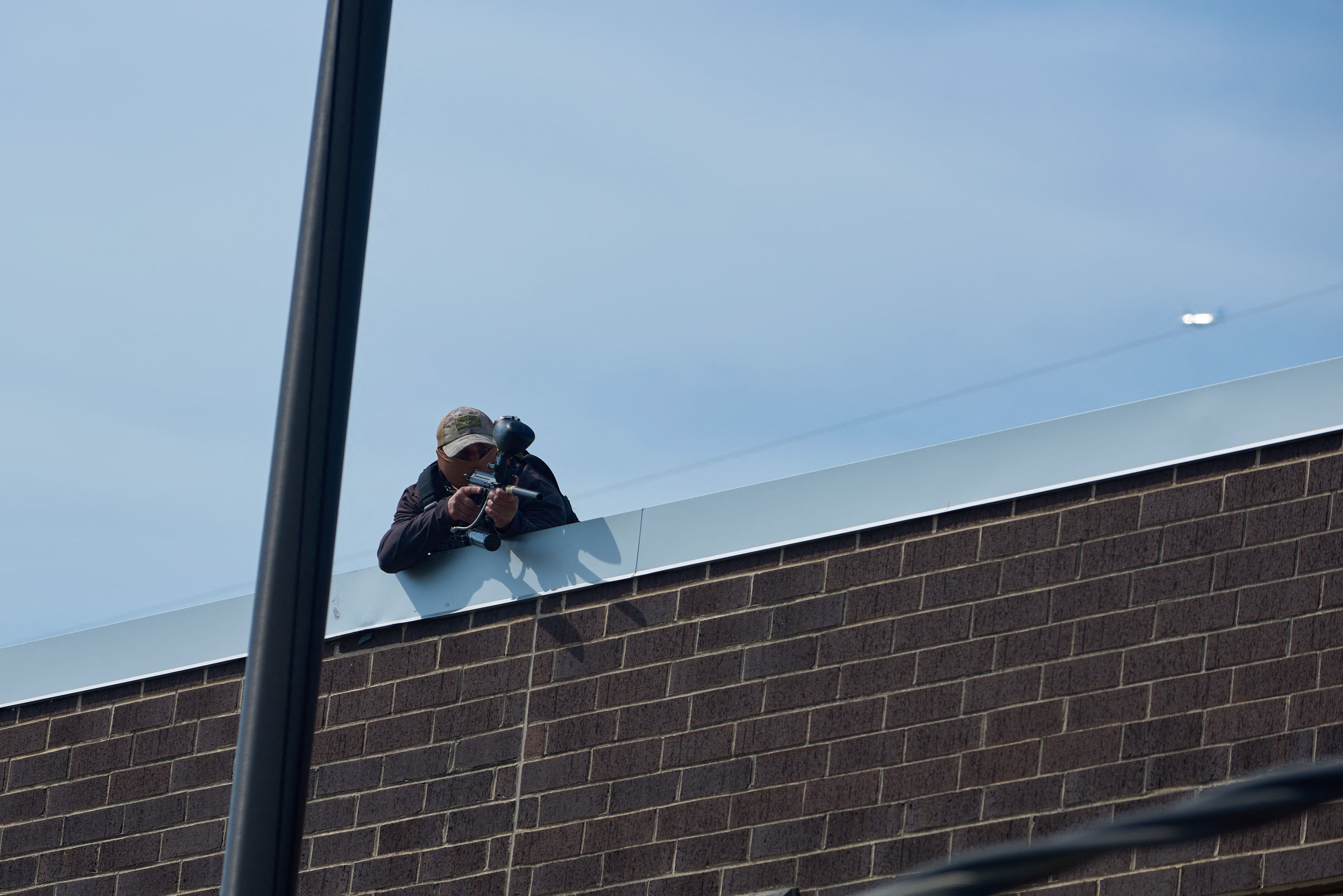 Photo of a man with a hat on top of a building pointing a gun down into a crowd. 