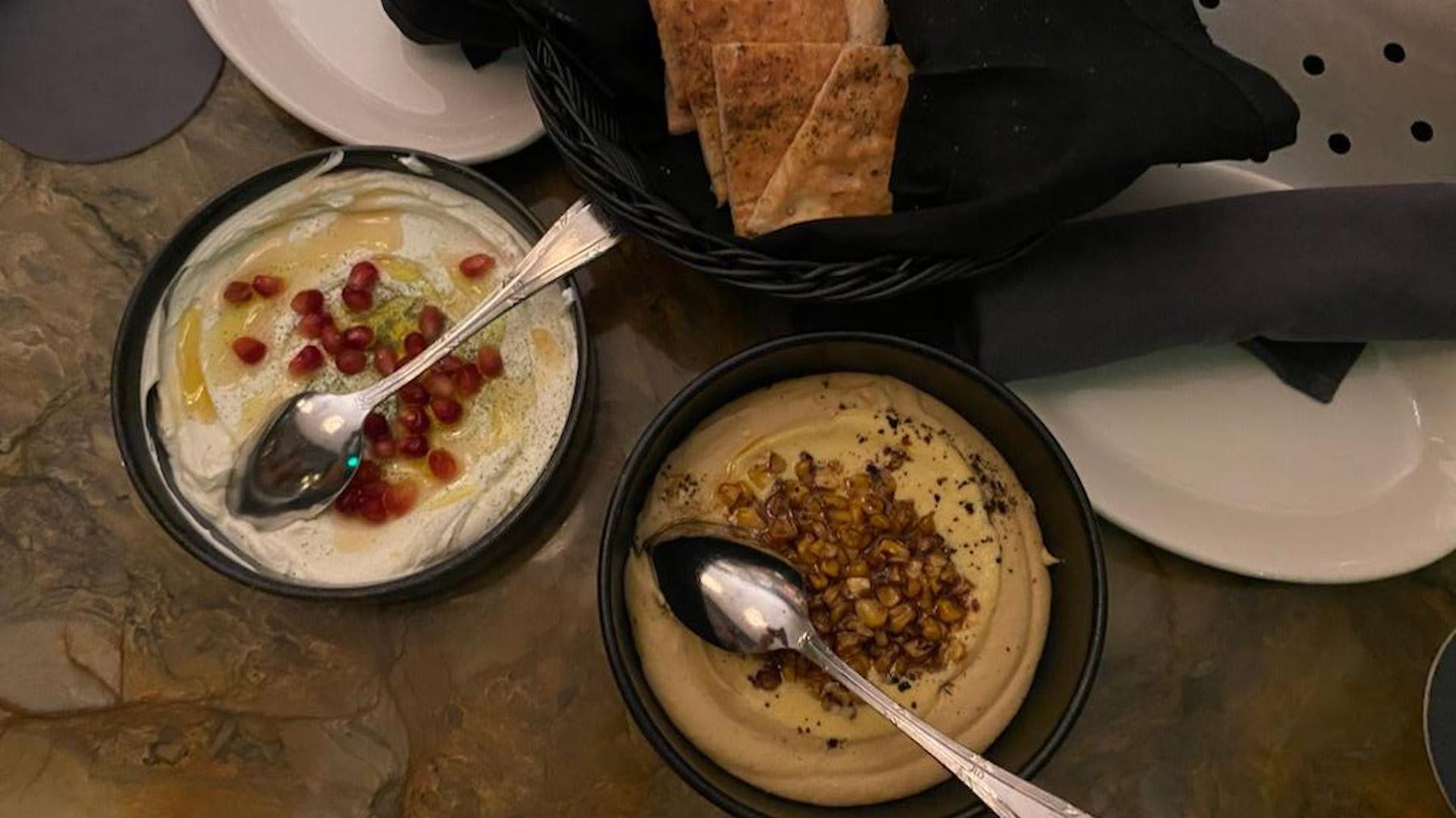 Two round dishes hold white labneh and yellowish hummus 