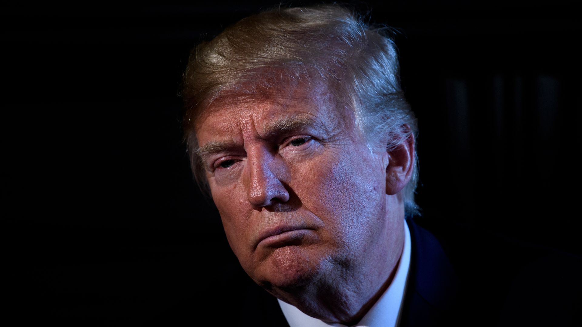 Donald Trump frowning in a dark room