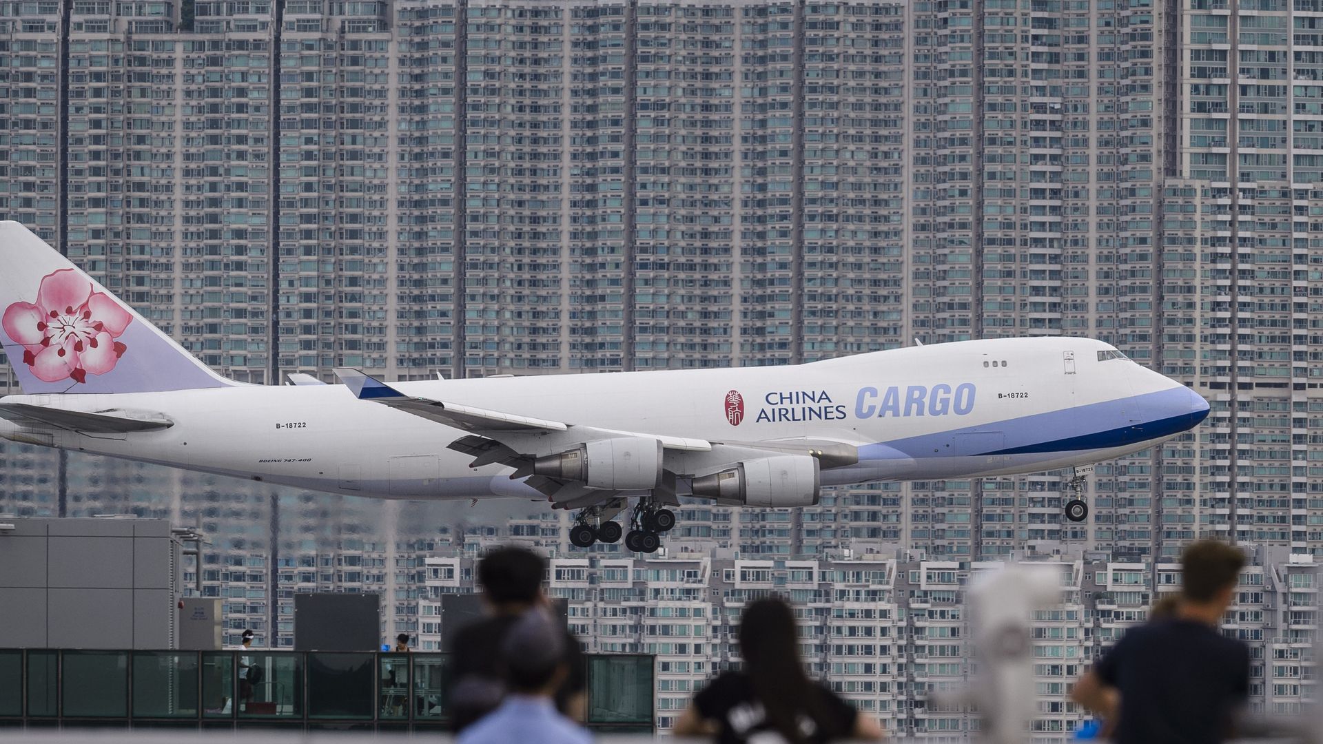 Photo of a landing cargo plane, in front of rows of high-rise buildings