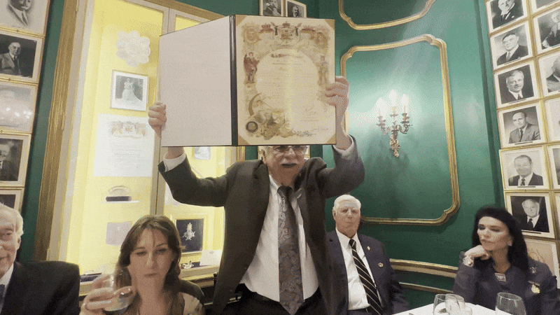 A man shows off a formal proclamation in a folder. He closes is and says "thank you."