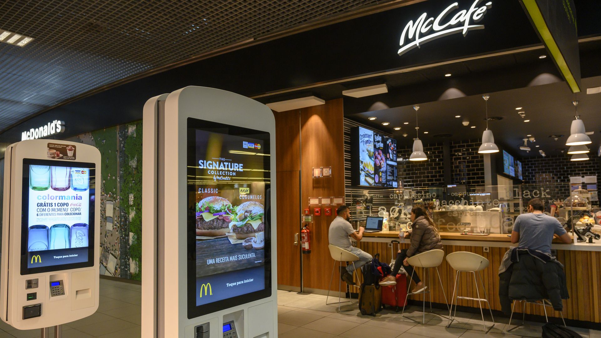 Travelers sit behind self service screens at fast food restaurant McDonald's in the passengers' lounge of Humberto Delgado International Airport in Lisbon, Portugal.