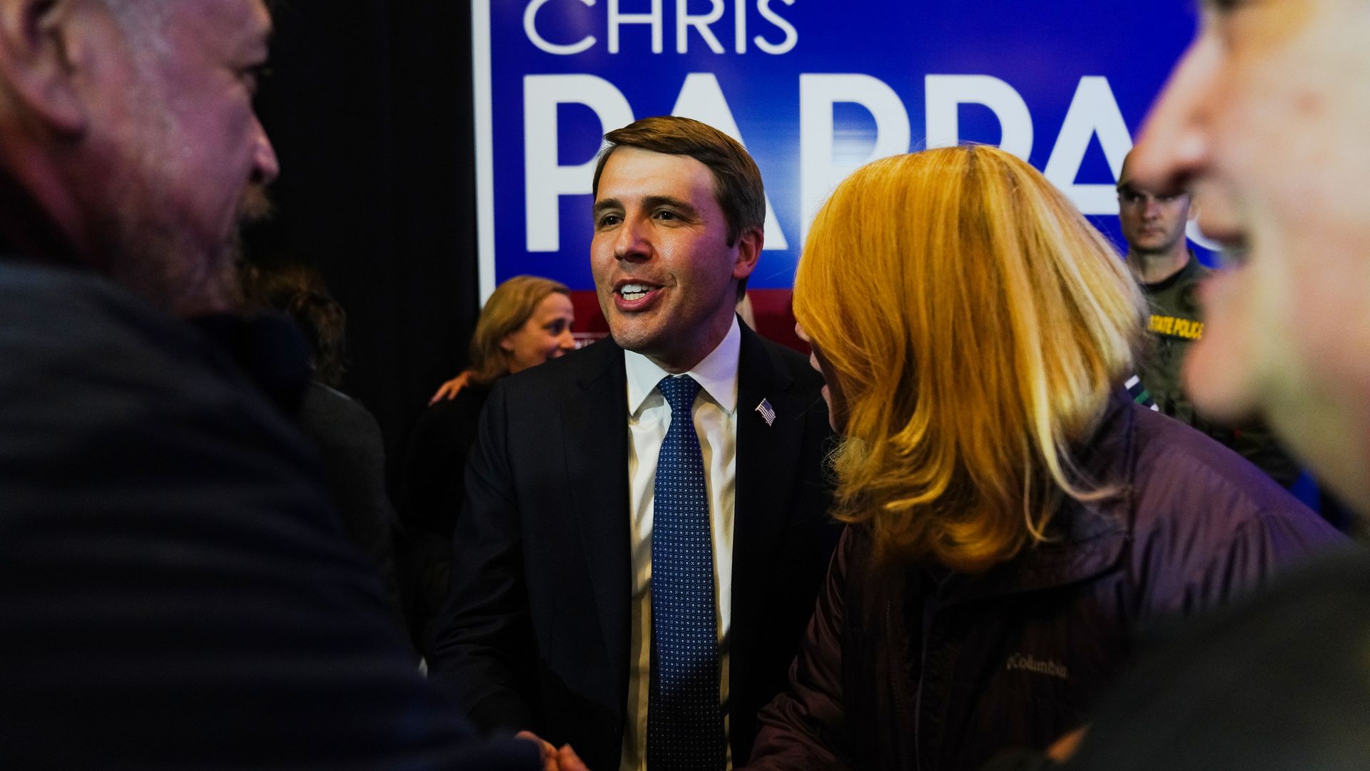 Rep. Chris Pappas, wearing a dark suit and shaking hands with supporters in front of a blue sign with his name on it.