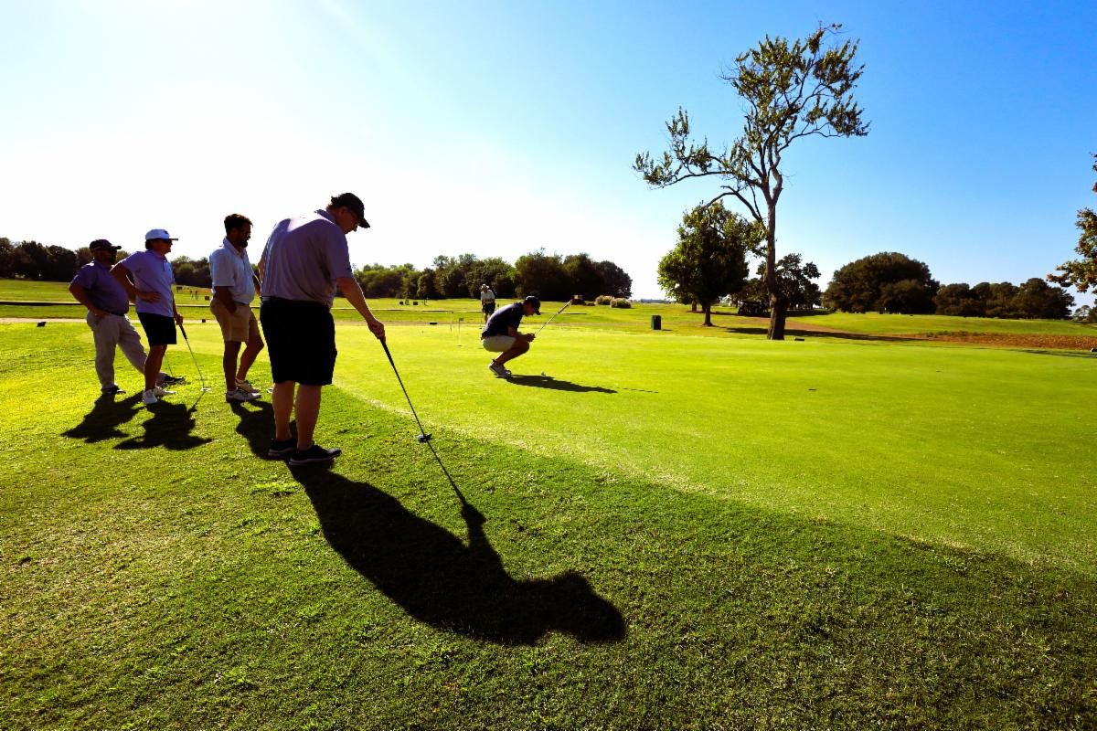 Golfers stand around a green, waiting on a fellow player to putt.
