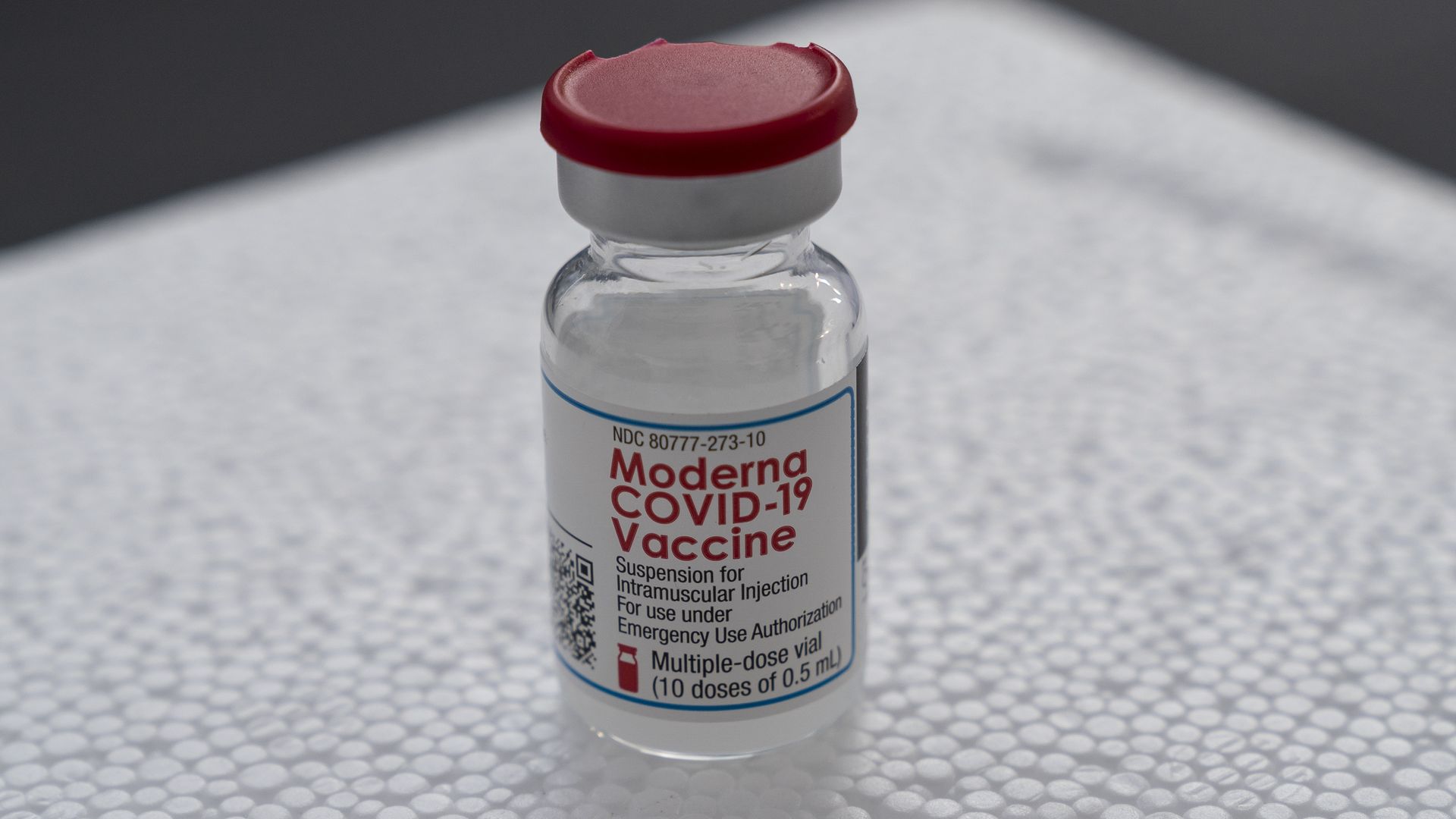 A clear vial with a red top containing the Moderna COVID-19 vaccine.