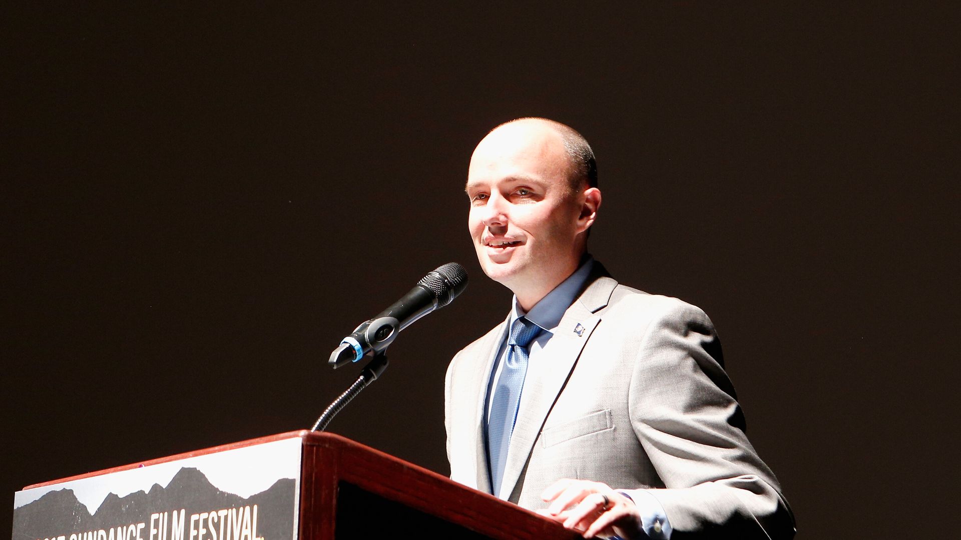 Utah Gov. Spencer Cox speaks at a podium under a spotlight.