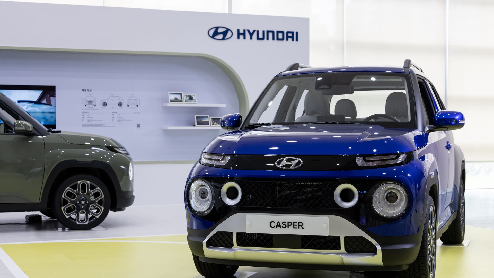 Photo of a blue Hyundai car on display on the right and a dark green Hyundai car on the left