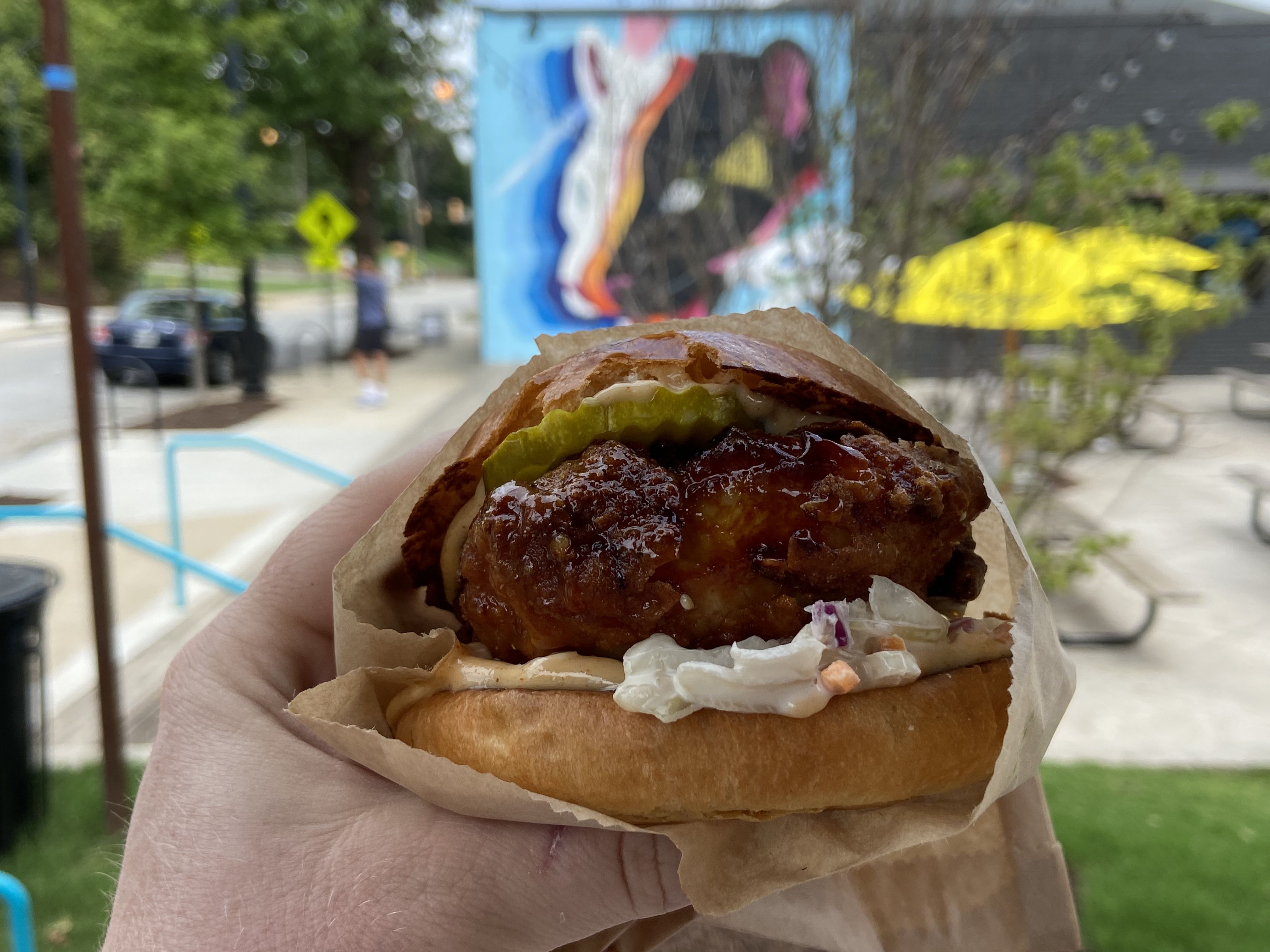A hand holds a large fried chicken sandwich with sesame slaw and a pillowy bun