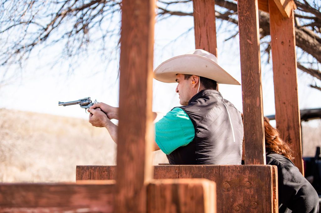 A man wearing a cowboy hat and shooting an old fashioned gun.