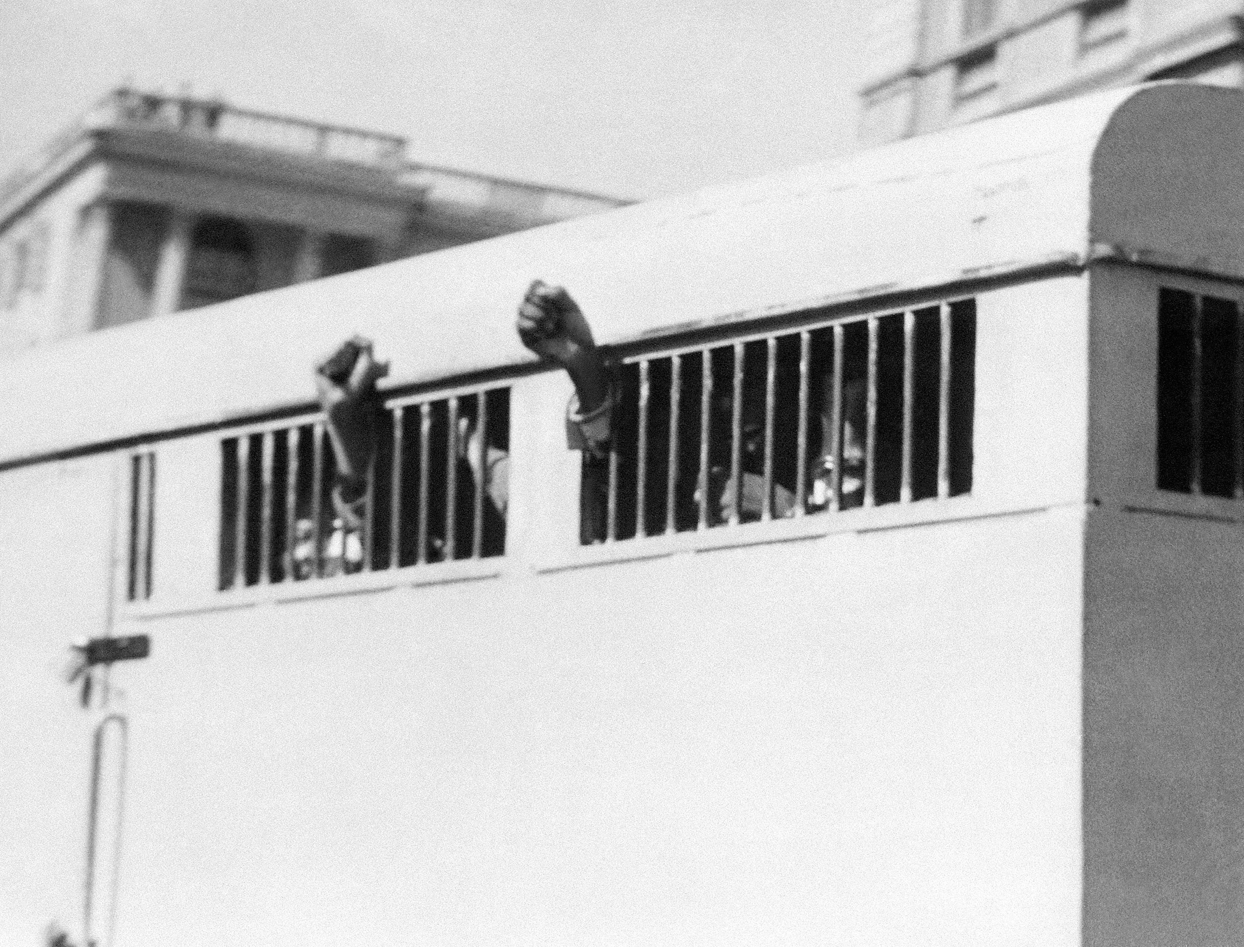 Eight men, among them anti-apartheid leader and African National Congress (ANC) member Nelson Mandela, sentenced to life imprisonment in the Rivonia trial leave the Palace of Justice in Pretoria 12 June 1964 with their fists raised in defiance through the barred windows of the prison car.