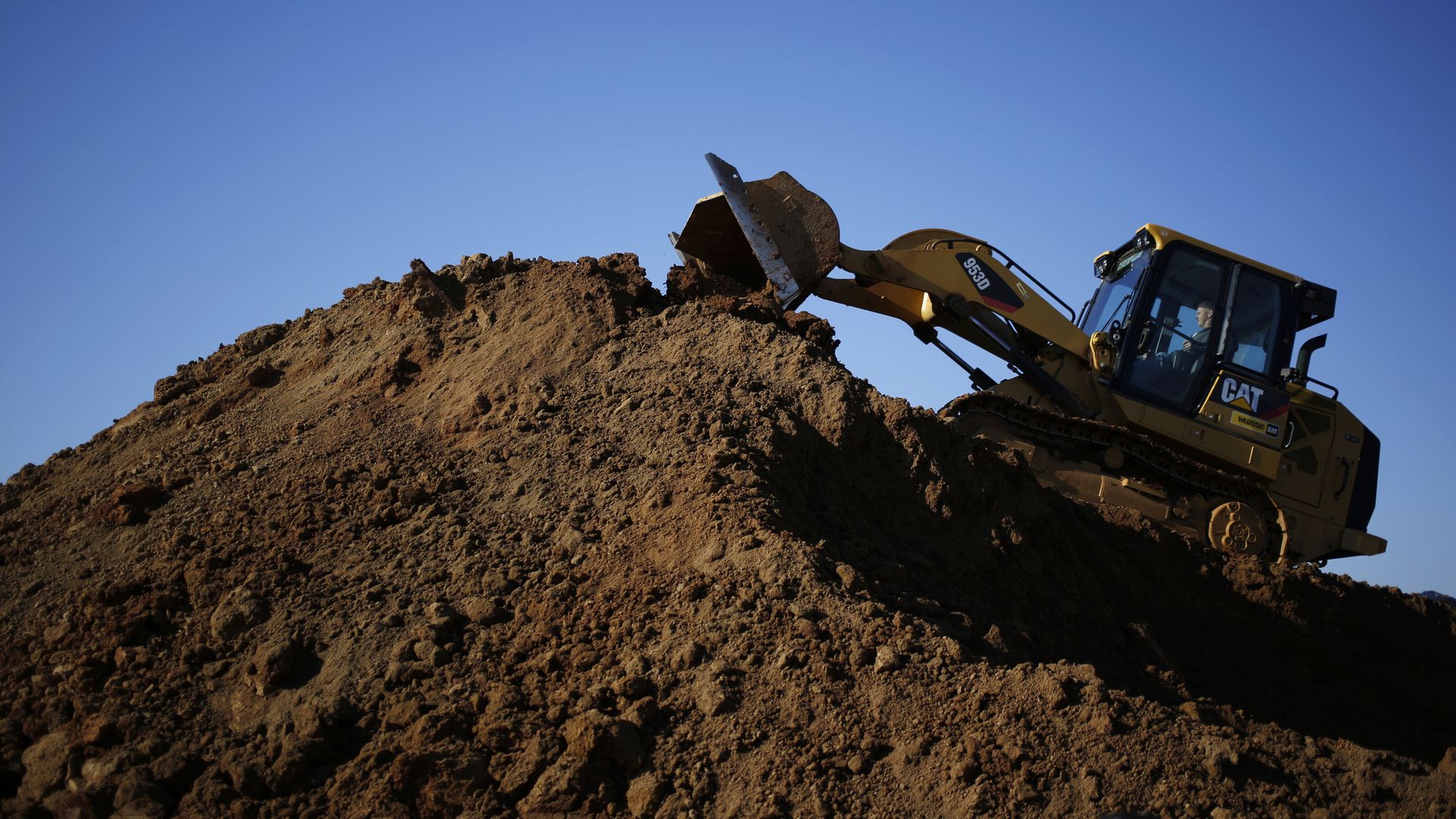 A construction vehicle hoists dirt on a mountain of soil