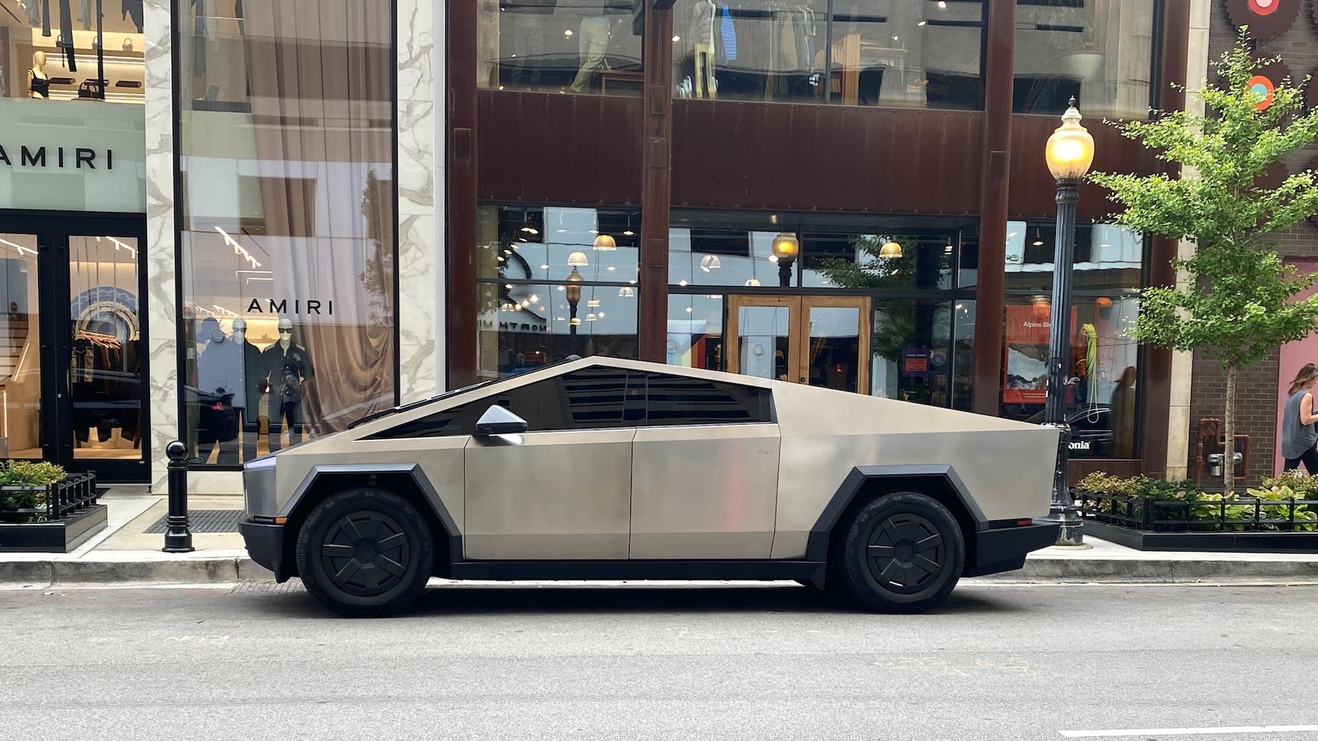 A stainless steel futuristic truck parked on a city street in front of stores.