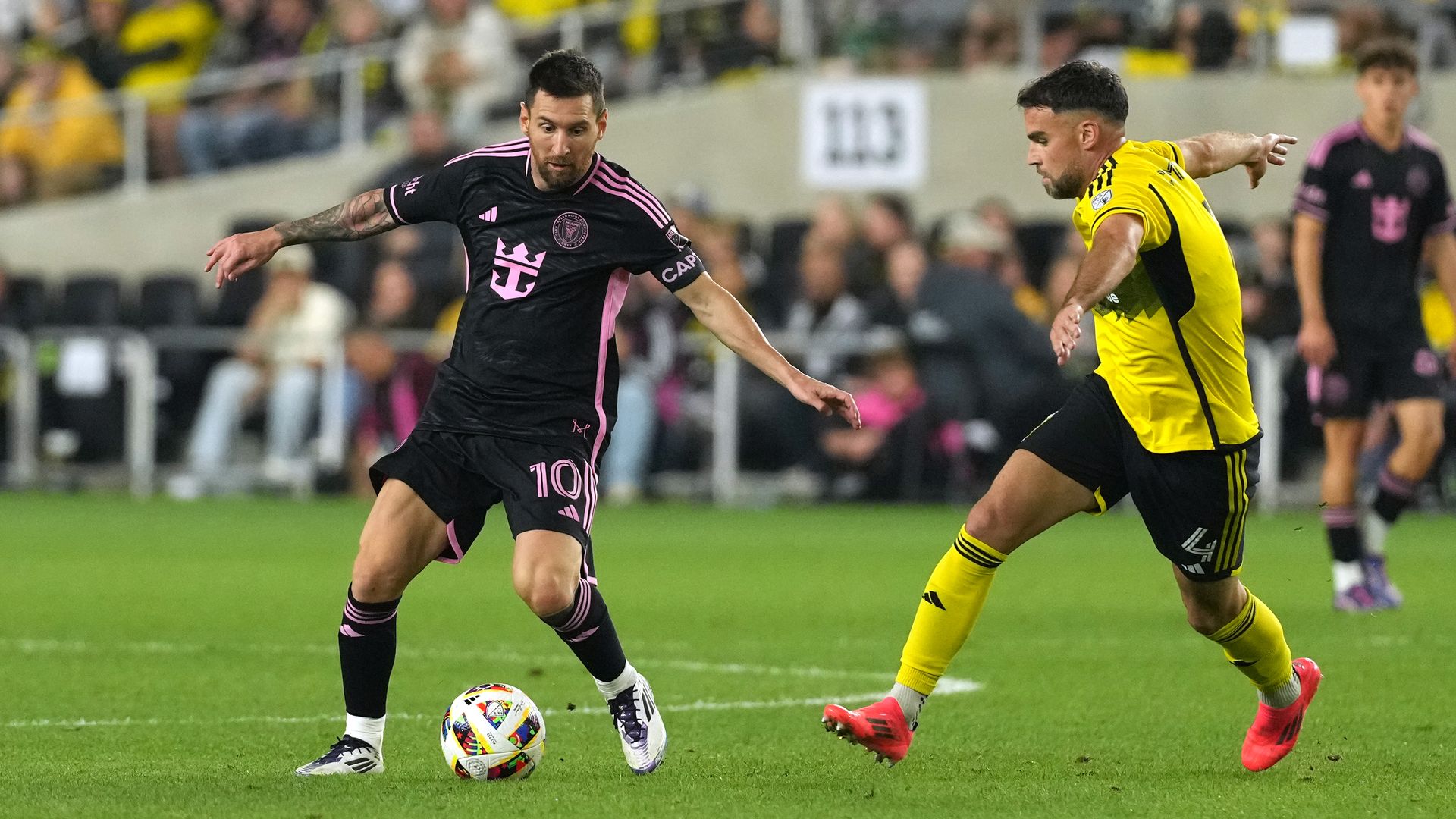 Lionel Messi in black jersey on soccer field against yellow jersey man