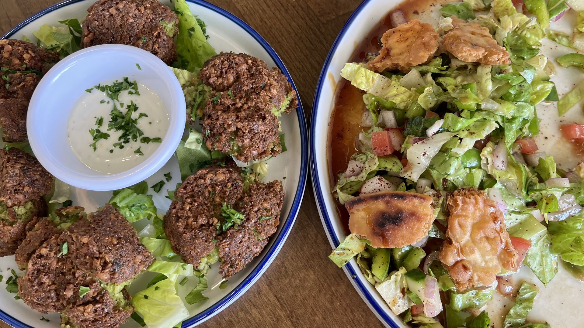 Two dishes pictured from above. On the left, a plate of textured brown discs. On the right, a salad with a dark brown dressing and fried pita.