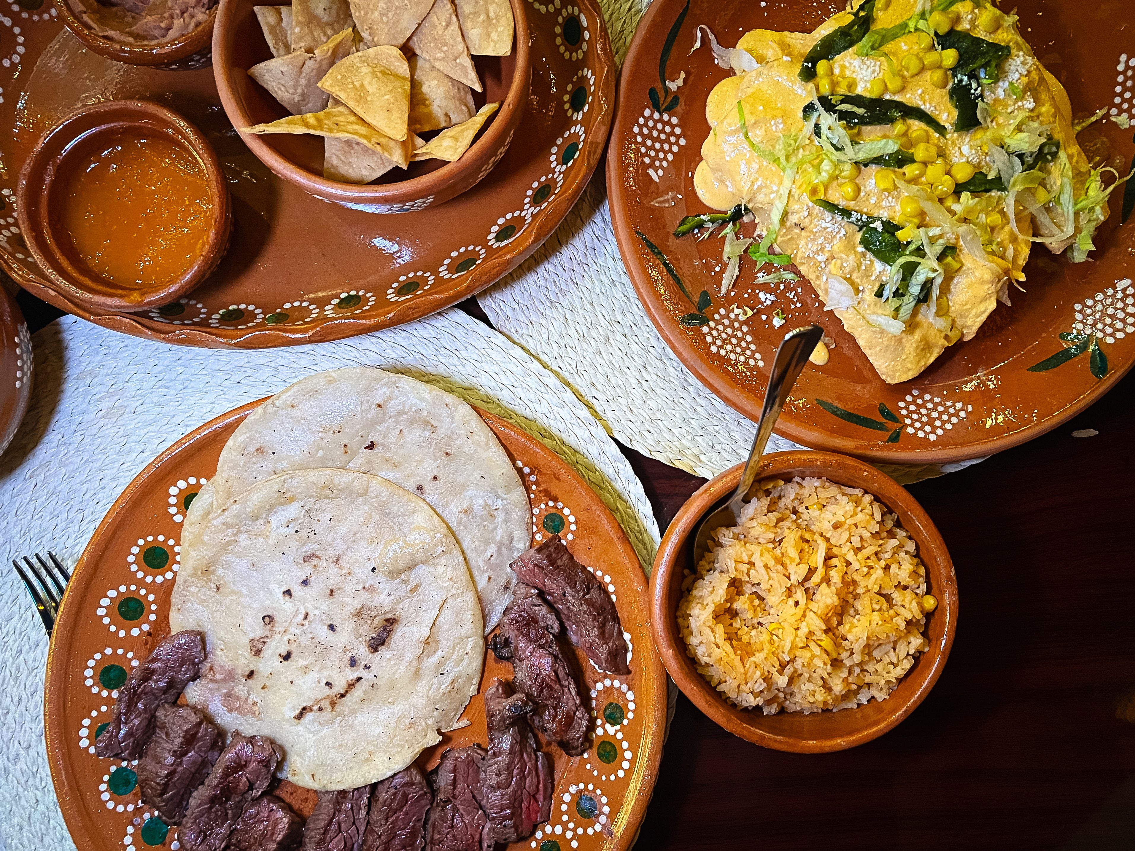 A spread of clay, decorated plates with dishes like enchiladas, fresh tortillas, rice, chips and salsa.