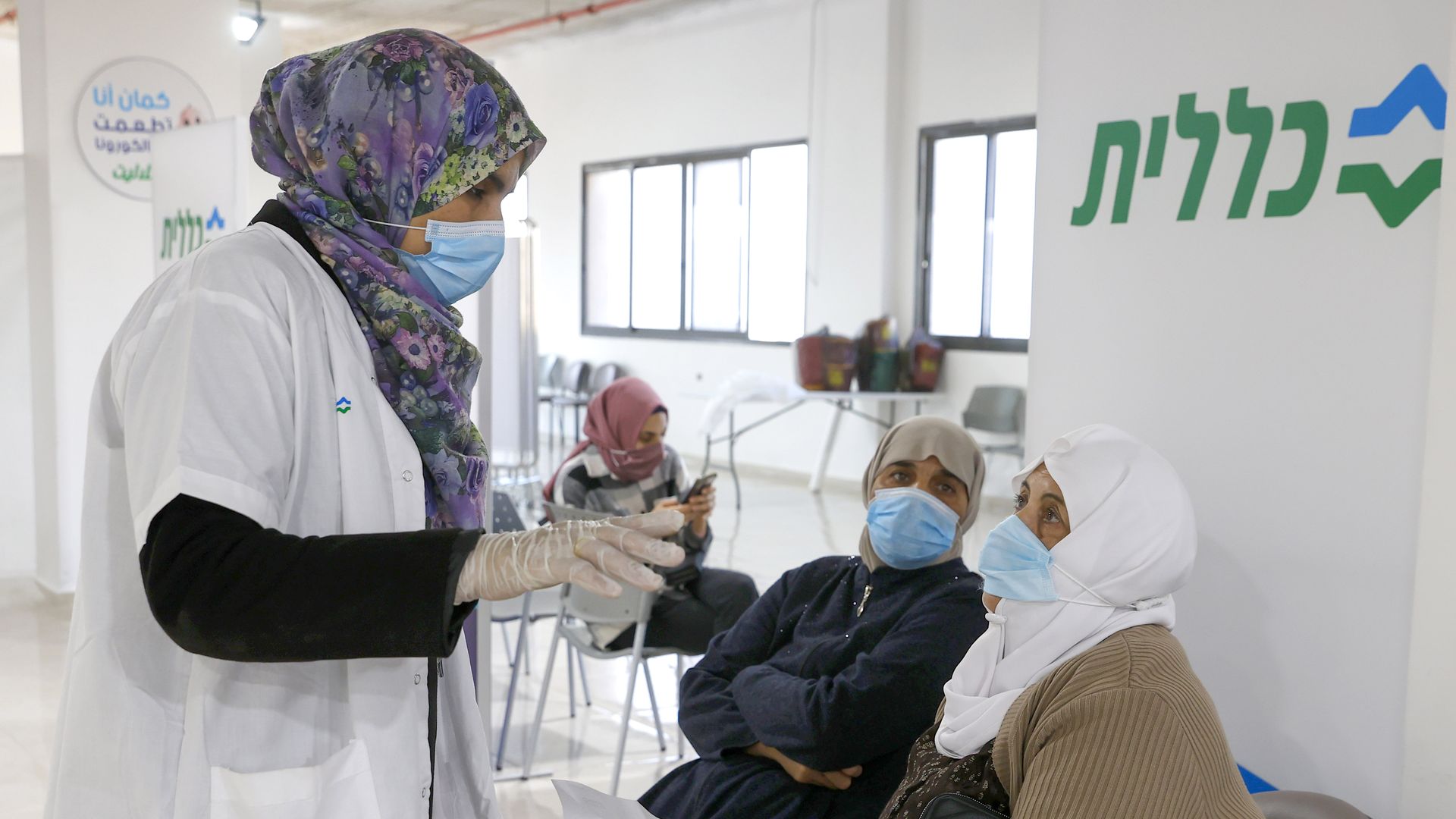 Photo of a masked healthcare worker speaking with two masked Arab Israeli woman in a hospital waiting room