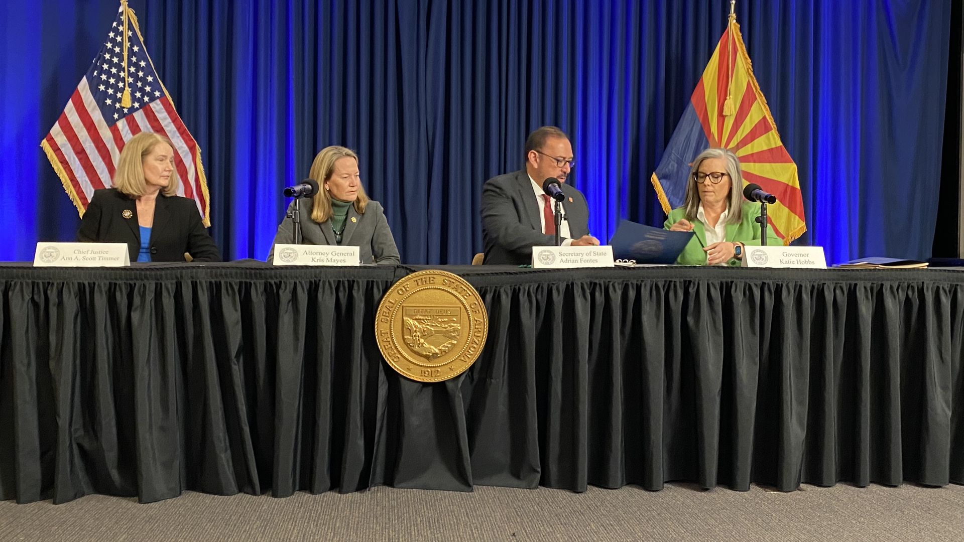 Ann Timmer, Kris Mayes, Adrian Fontes and Katie Hobbs sit at a table signing paperwork. 