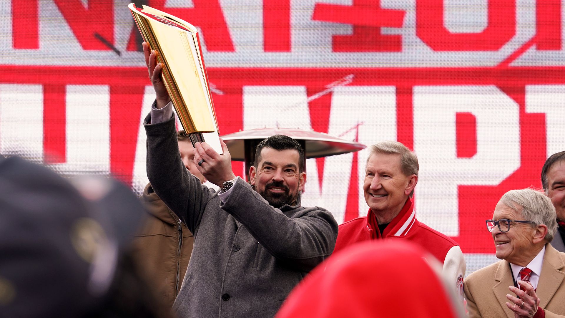 Ohio State head coach Ryan Day lifts the College Football Playoff National Championship Trophy during a celebration at Ohio Stadium alongside OSU president Ted Carter and Ohio Gov. Mike DeWine