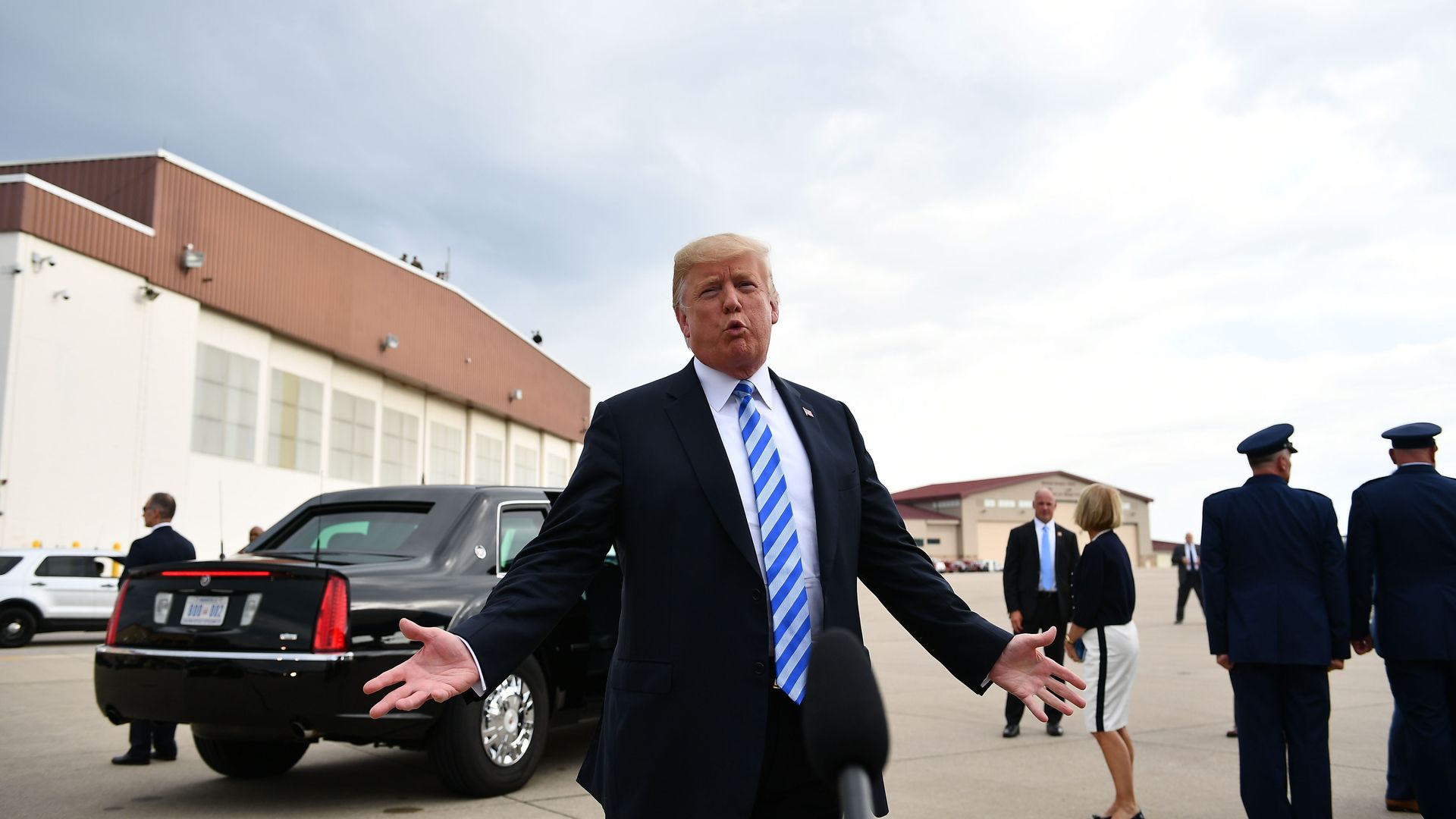 Donald Trump standing in front of a limo with his hands slightly out to the side talking to the press with his mouth in a "O" shape