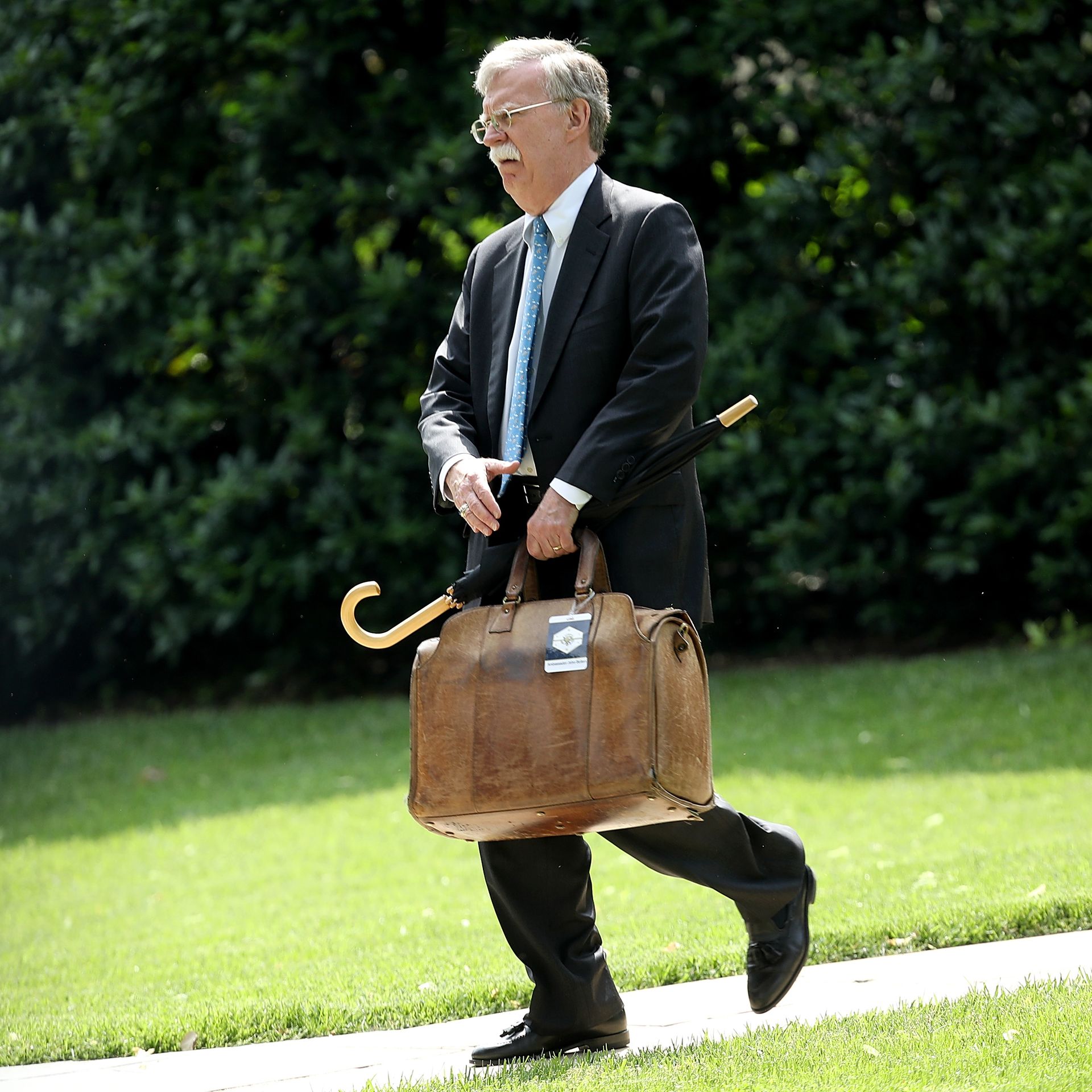 John Bolton carrying luggage and umbrella